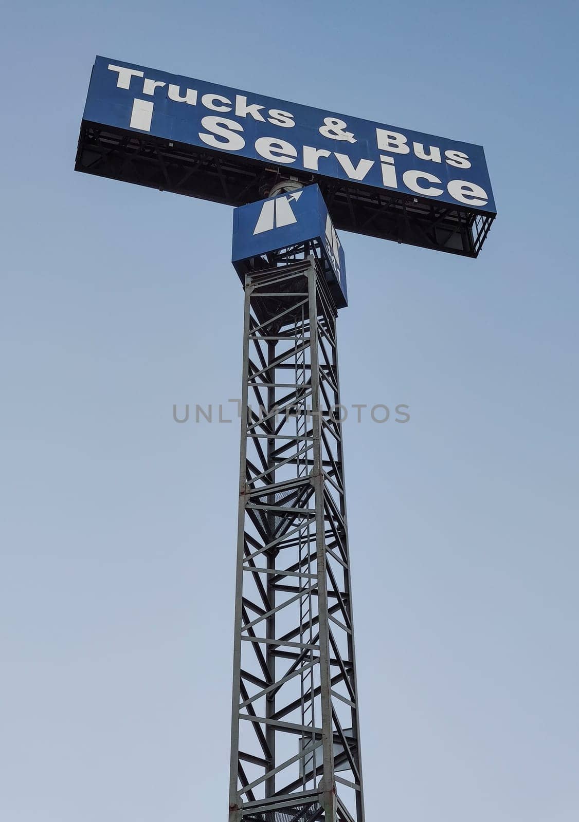 Trucks and bus service sign pole over blue sky.