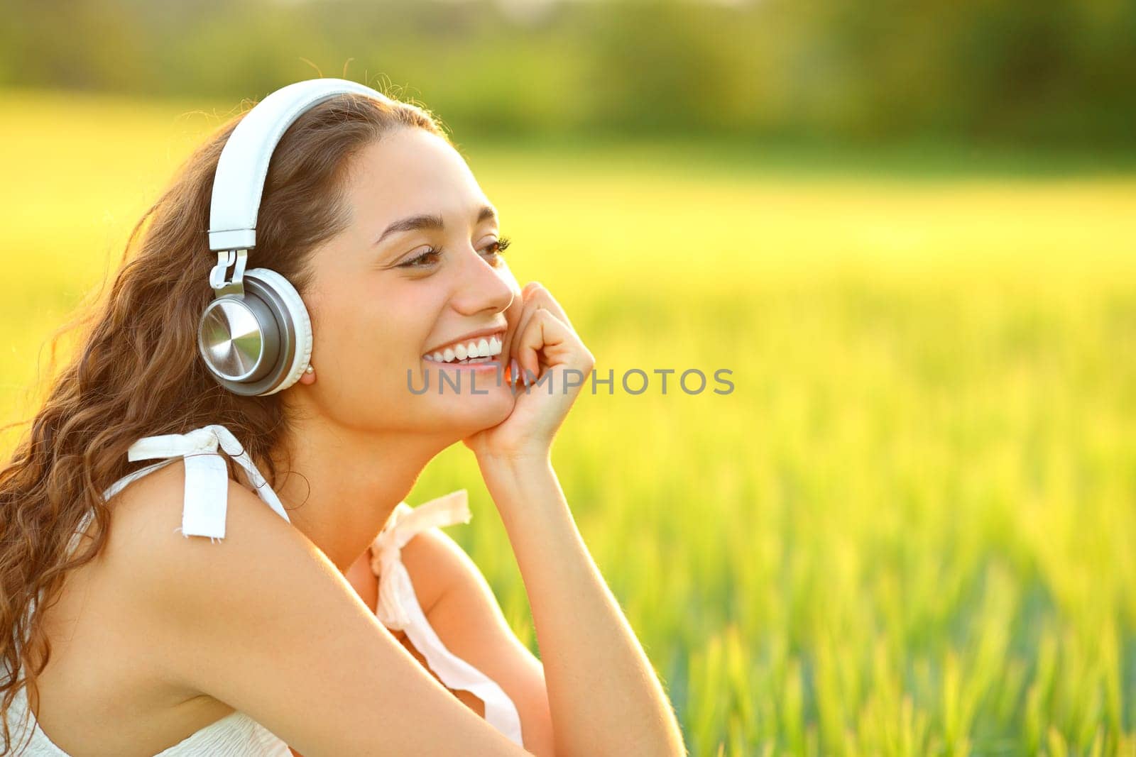 Happy woman listening to music with wireless headphones sitting in a wheat field