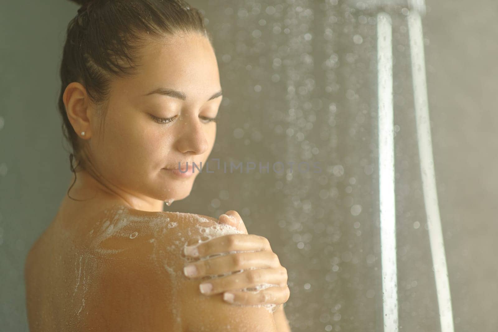 Beautiful woman soaping shoulder in a shower under water jet