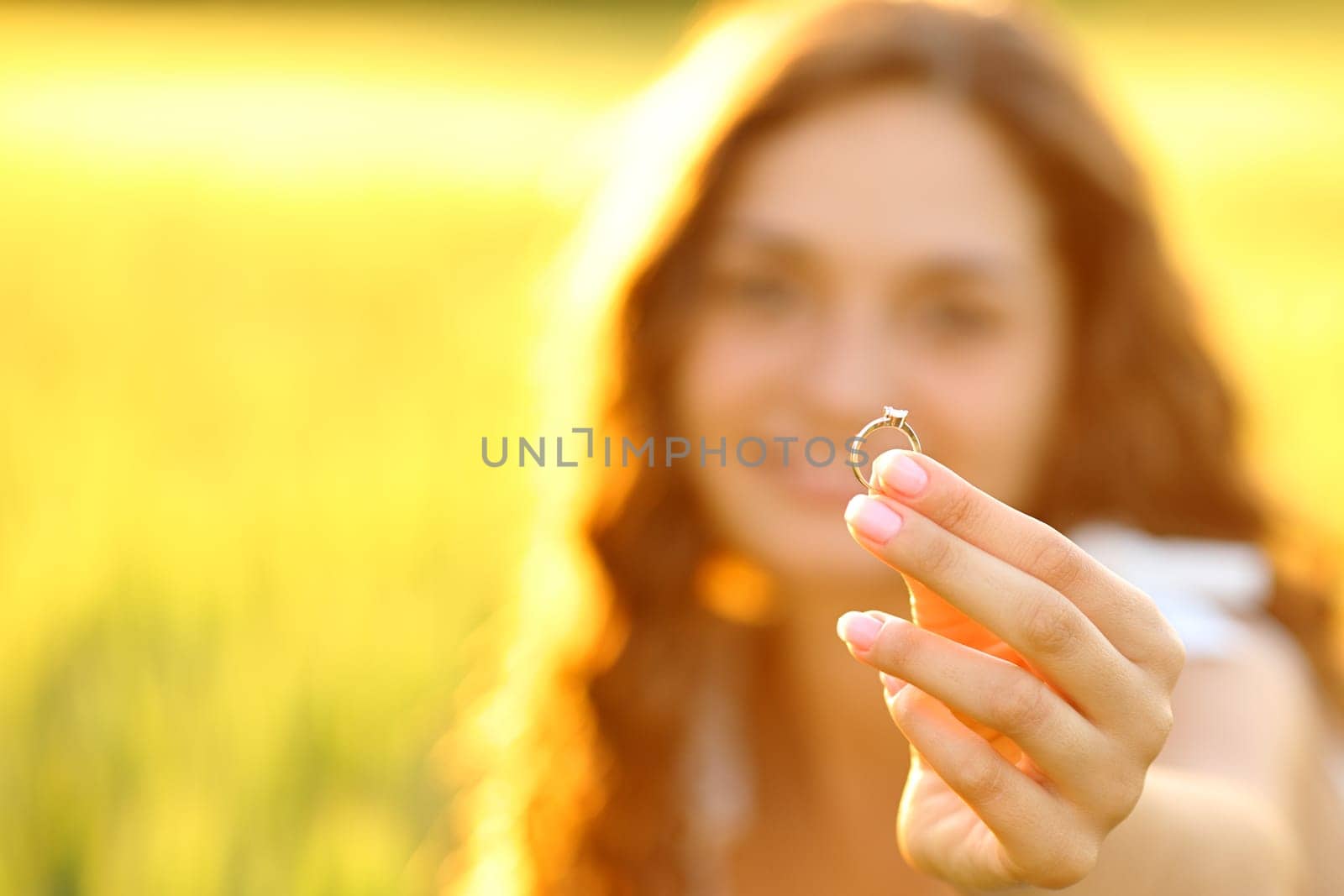 Close up portrait of a happy woman showing her engagement ring at sunset in a field