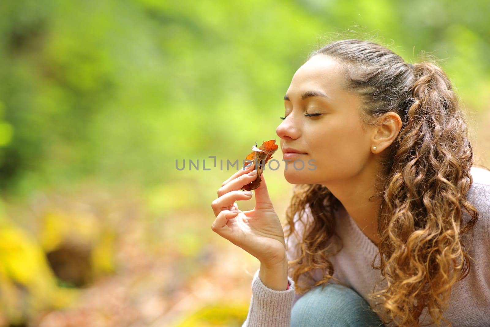 Happy woman smelling dead leafs in a forest