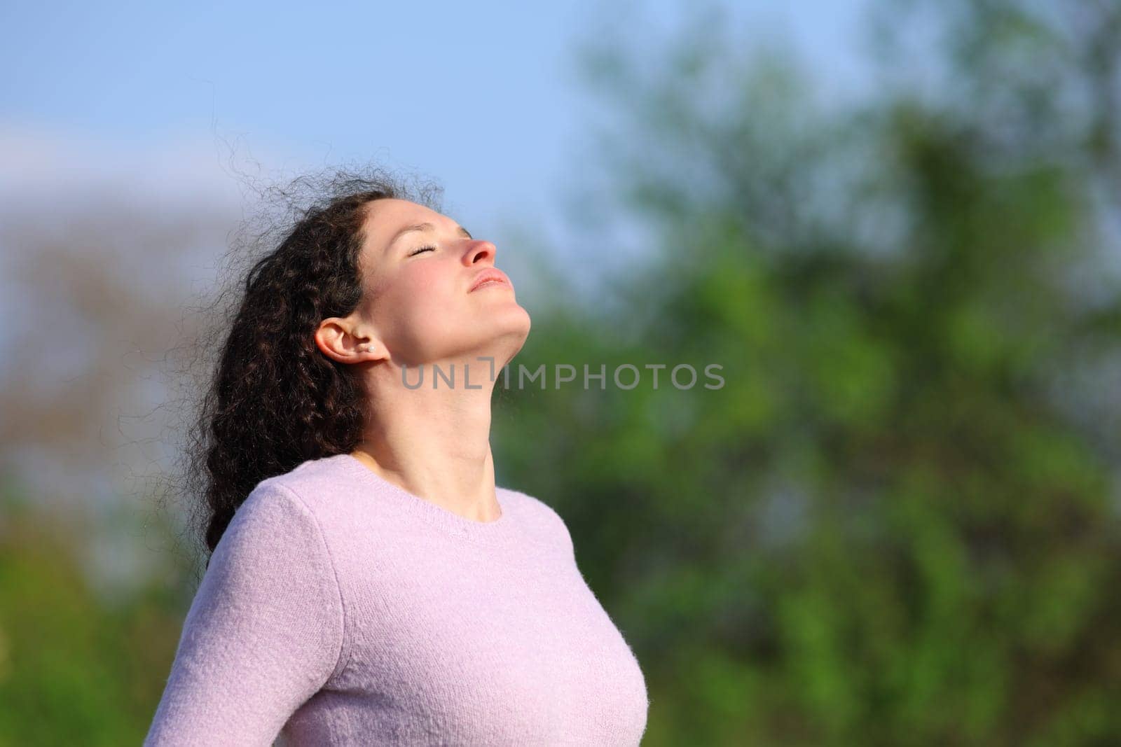 Woman with curly hair breaths fresh air in a park