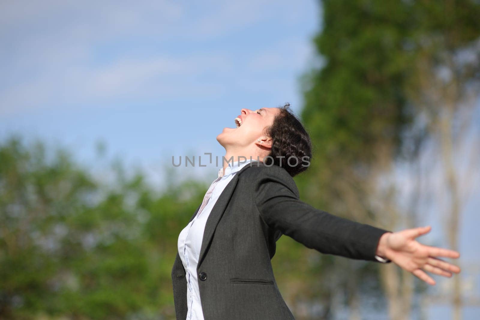 Side view portrait of an excited businesswoman outstrstching arms in a park
