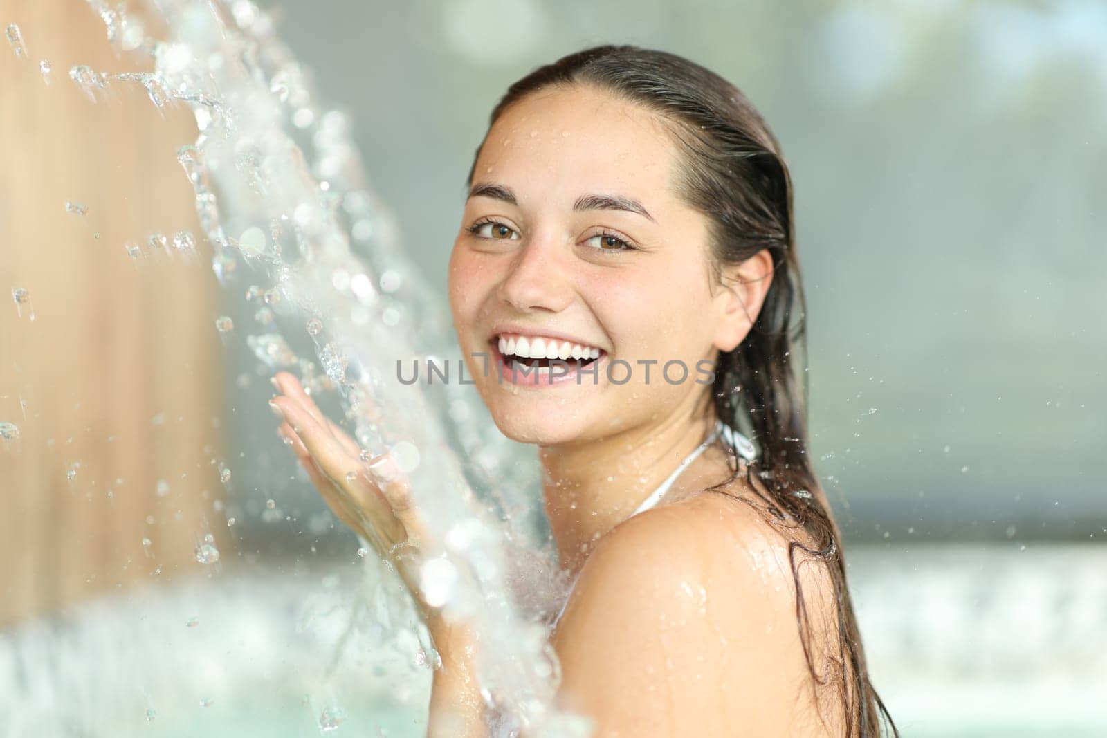 Happy woman bathing in spa under water jet looking at camera