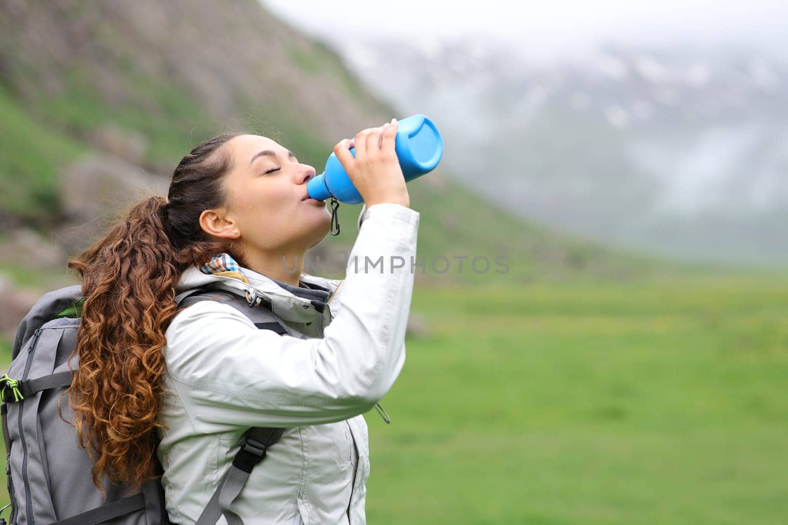 Trekker drinking water from canteen standing alone in the mountain a foggy day