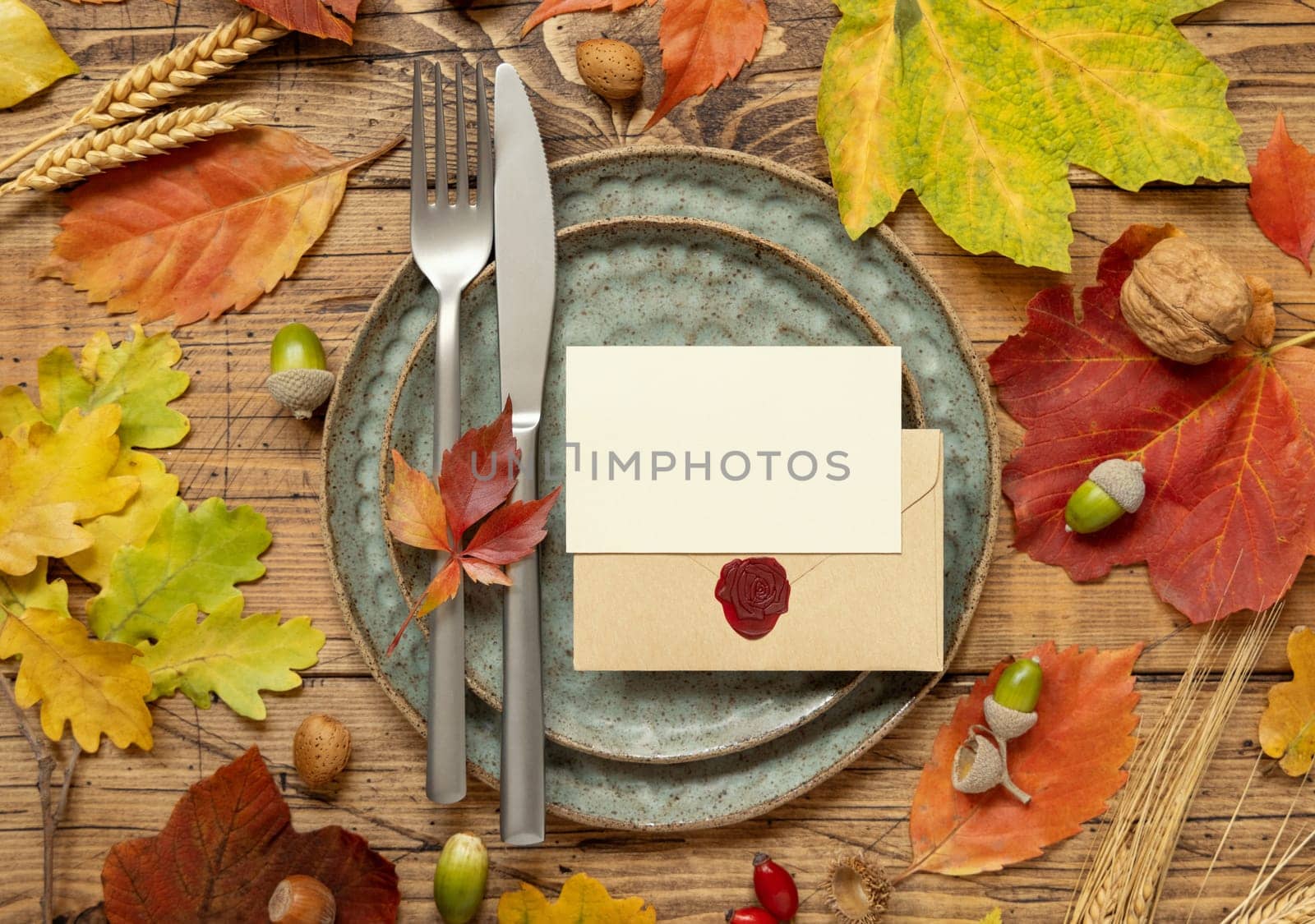 Autumn rustic table setting with blank place card and envelope between colorful leaves and berries, top view, mockup. Flat lay Horizontal card on wooden table, flat lay, copy space. Thanksgiving or harvest