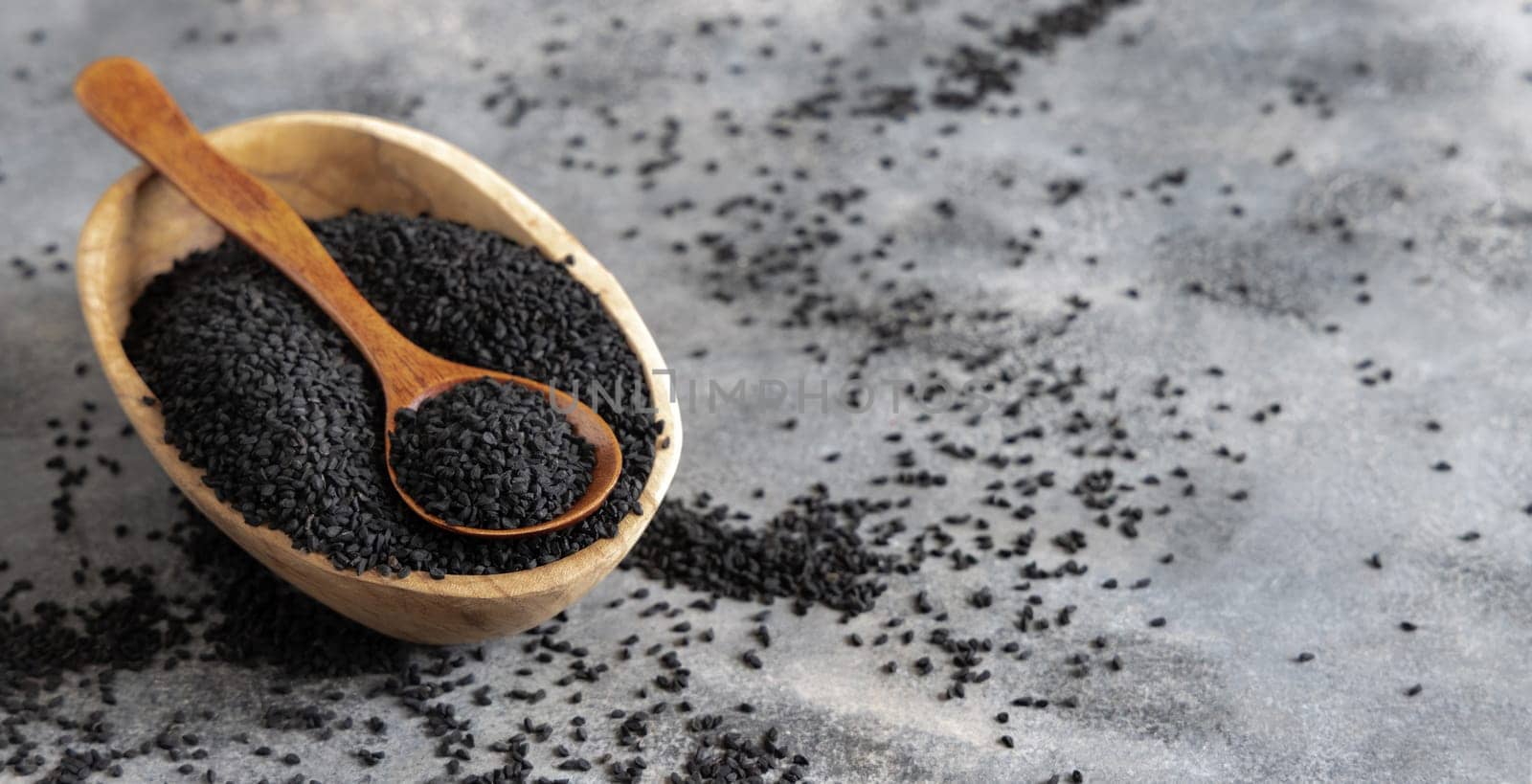 Indian spice Black cumin (nigella sativa or kalonji) seeds in bowl with spoon on grey table close up with copy space. Traditional medicine, healthy and vegetarian food concept.