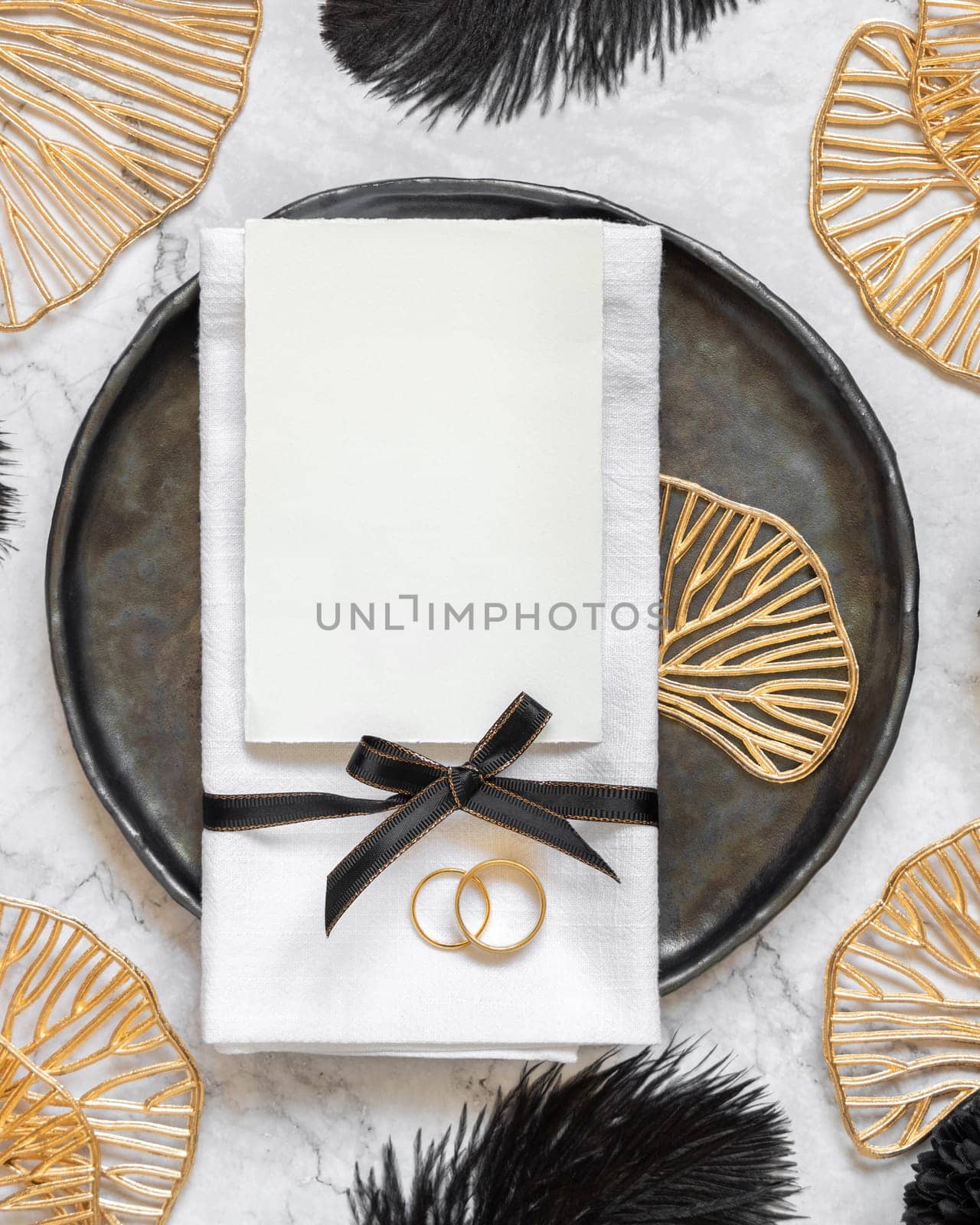 Black and golden wedding table setting with a blank card and rings top view, mockup. Elegant flat lay with vertical Invitation paper card, wedding or holiday stationery template