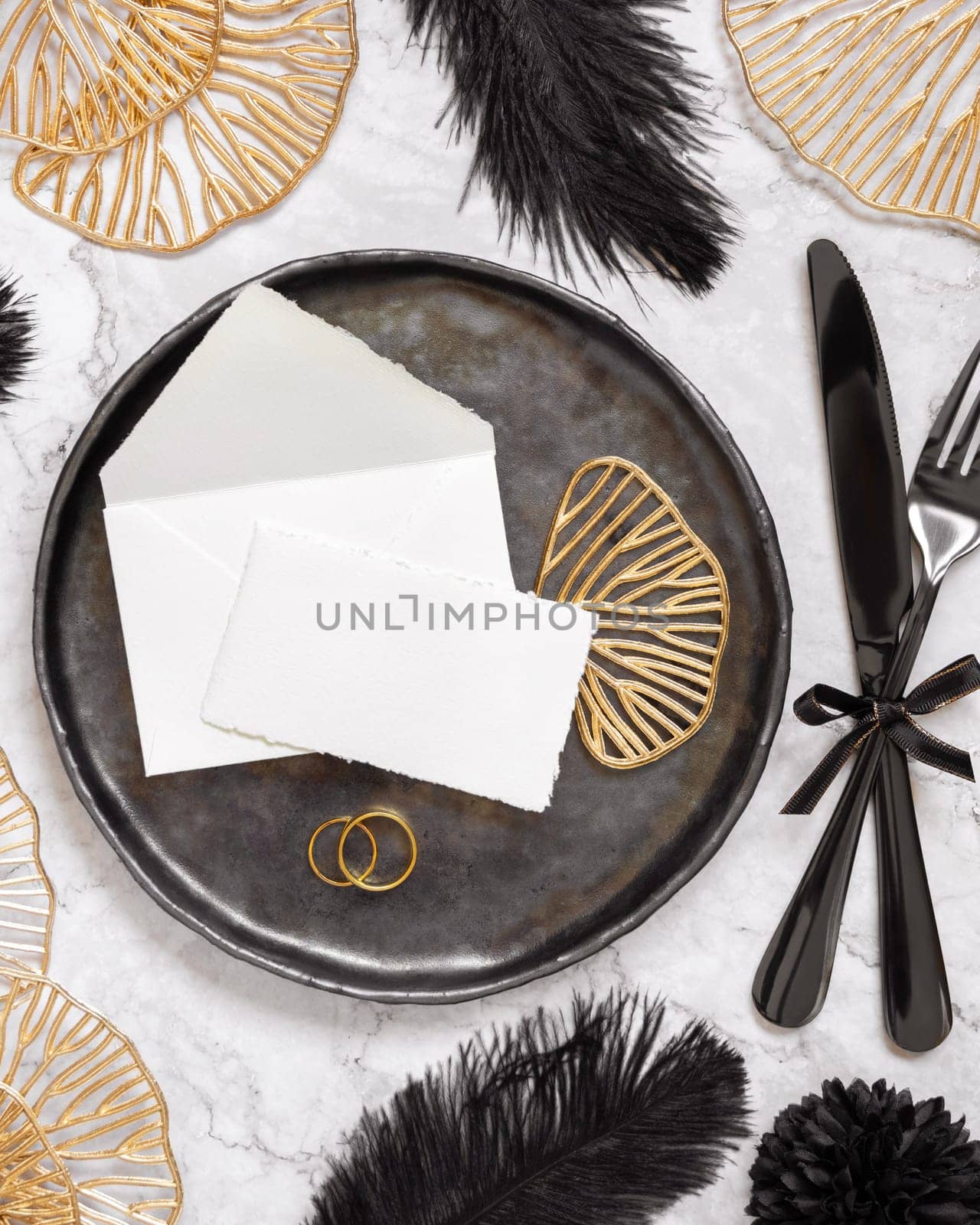 Black and golden wedding table setting with a place card and rings top view, mockup. Elegant flat lay with paper card and envelope, wedding or holiday stationery template
