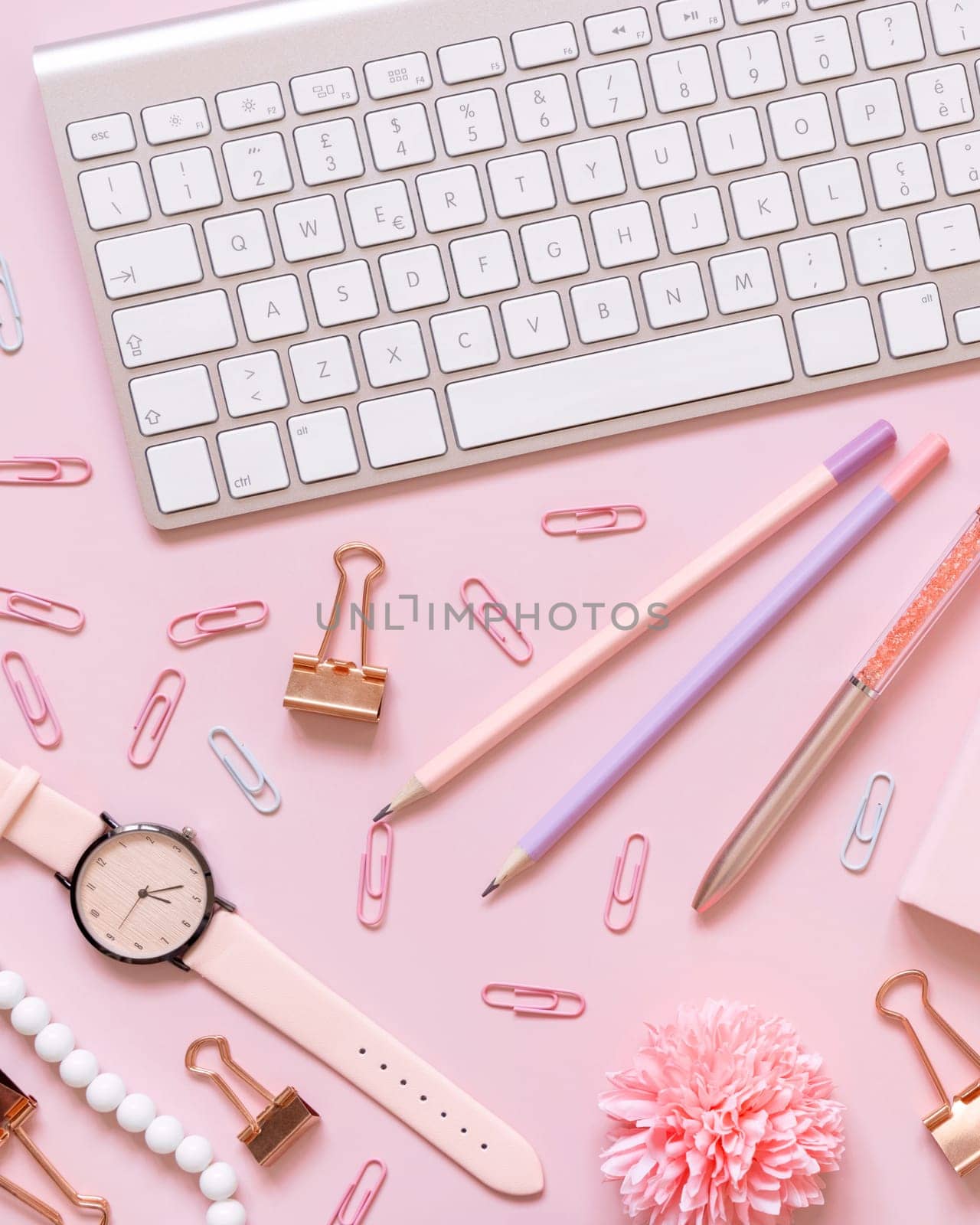 Keyboard and Pink school accessories on light pink, Top view. Girly workplace with flowers, Keyboard, pencil, pen and watch. Back to school