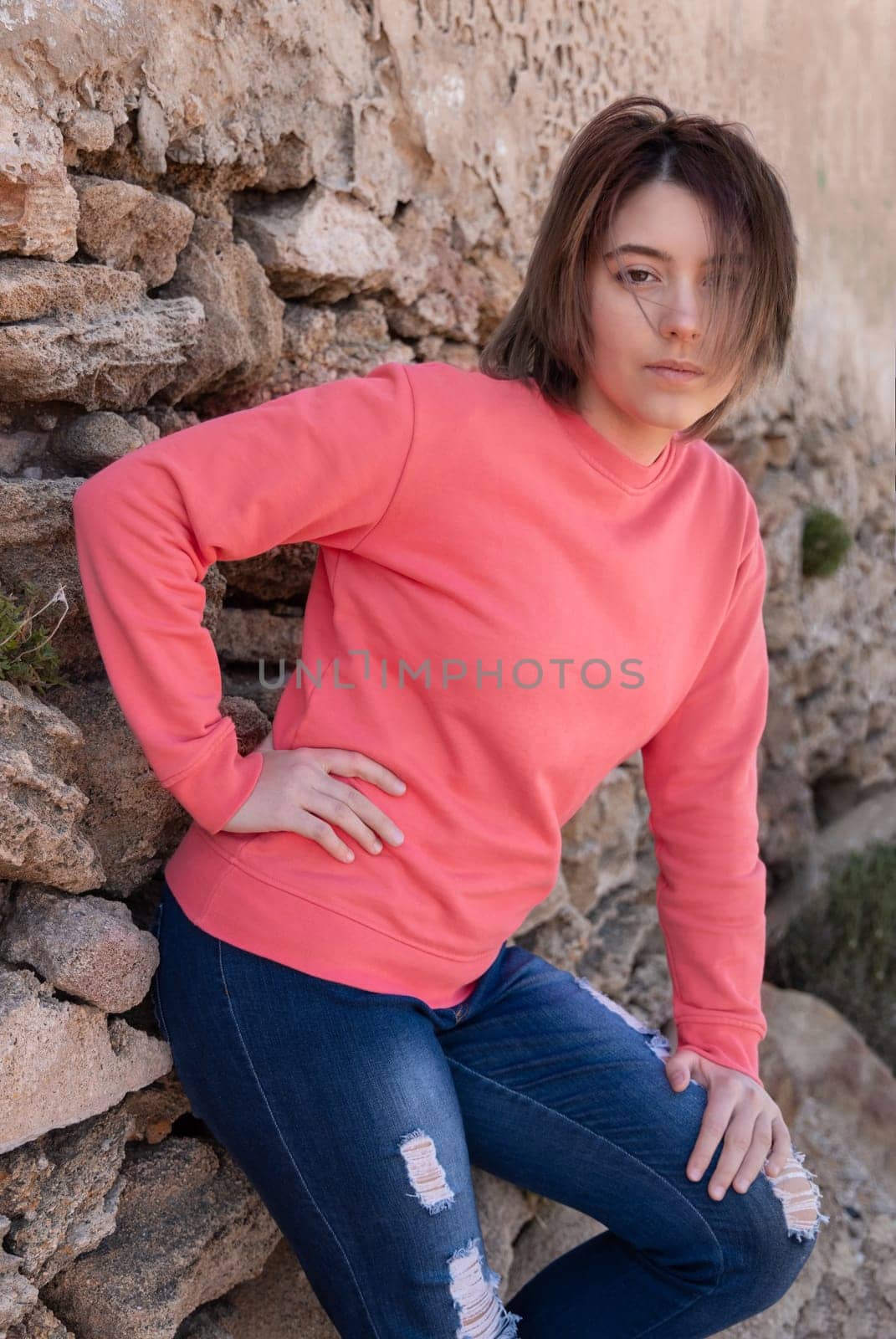 Teen girl wearing pink long sleeve shirt looking into a camera. Mockup. Serious Teenager girl standing outdoor near a wall, spending her time alone. Adolescence concept