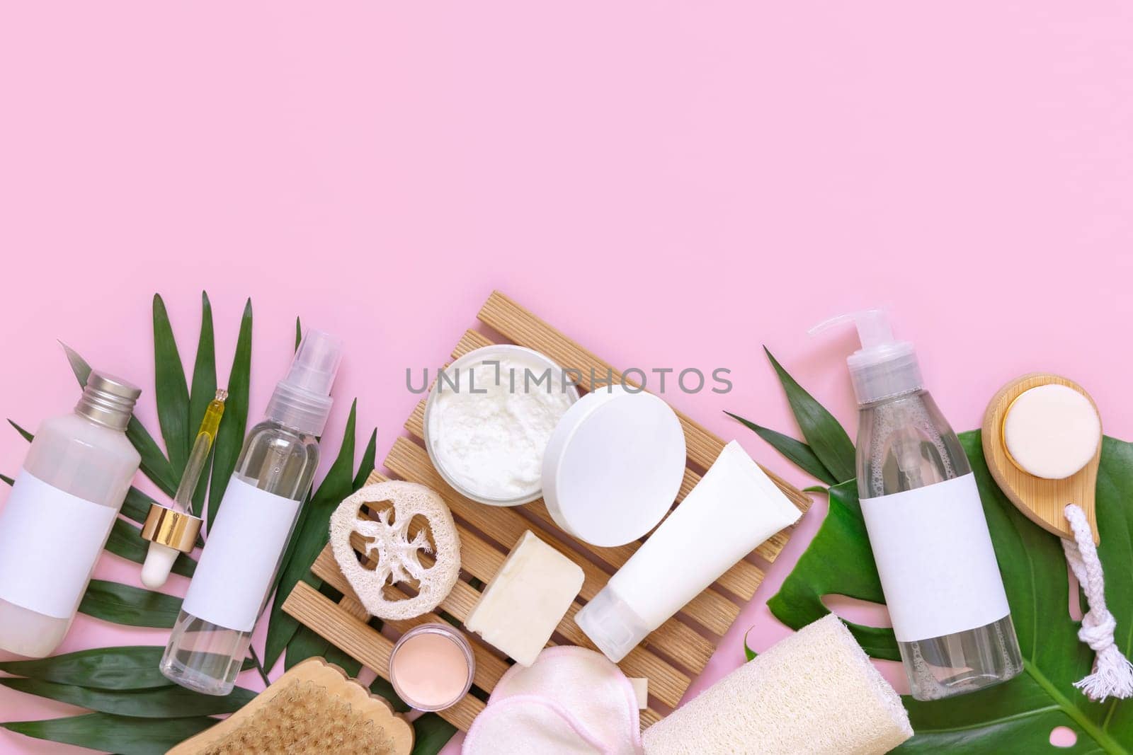 Homemade Cosmetics and accessories on tropical leaves on pink flat lay, copy space. Brand package mockup. Natural beauty products for hair and skin care, Top view
