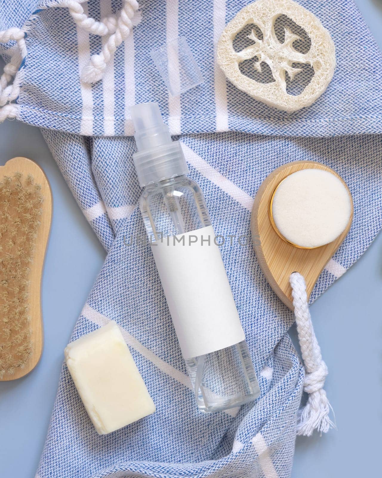 Refillable Spray bottle, skin and hair care accessories on blue bath towel near tropical leaves top view, copy space. Packaging mockup. Natural homemade products