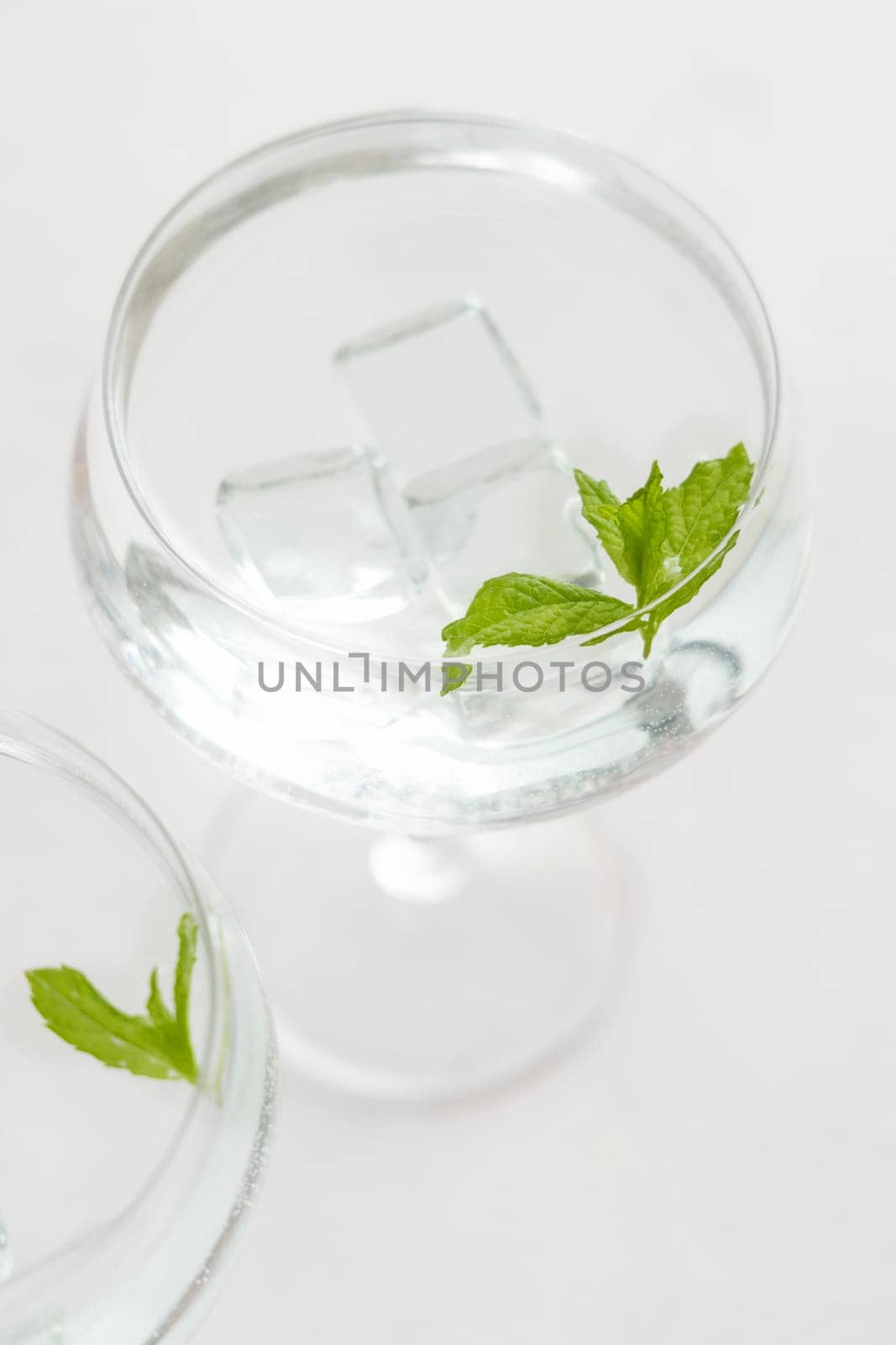 Transparent cocktail with ice cubes in a glass decorated with mint leaves close up. Tropical drink at the bar. Summer vacation mood. Analcolic mocktail drink