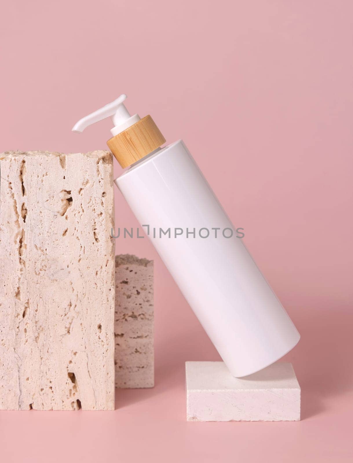 White one pump bottle lies on travertine stone on light pink, close up, mockup. Skincare beauty product. Natural cosmetics, lotion or cleanser. Minimal composition..
