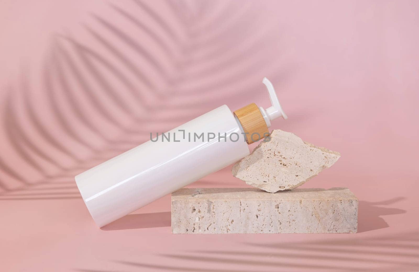 White one pump bottle lies on stone on light pink, palm leaf hard shadow behind, close up, mockup. Skincare beauty product. Natural cosmetics, lotion or cleanser. Minimal composition..