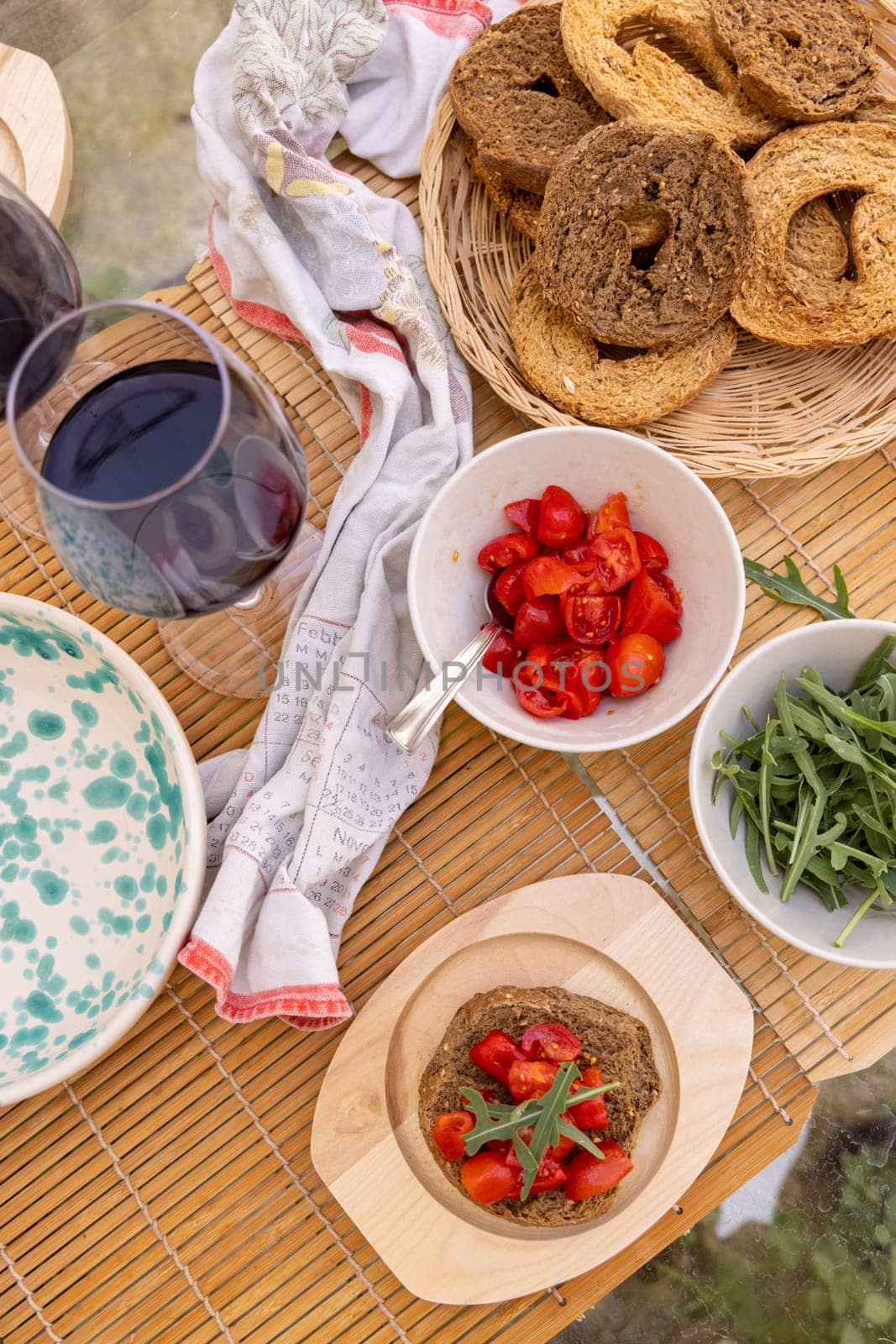 Italian summer appetizer Friselle with cherry tomatoes, oil and rucola served outdoor with glasses of red wine. Tipical Apulian Dried bread, made in Salento. Local cousine. Vegetarian food