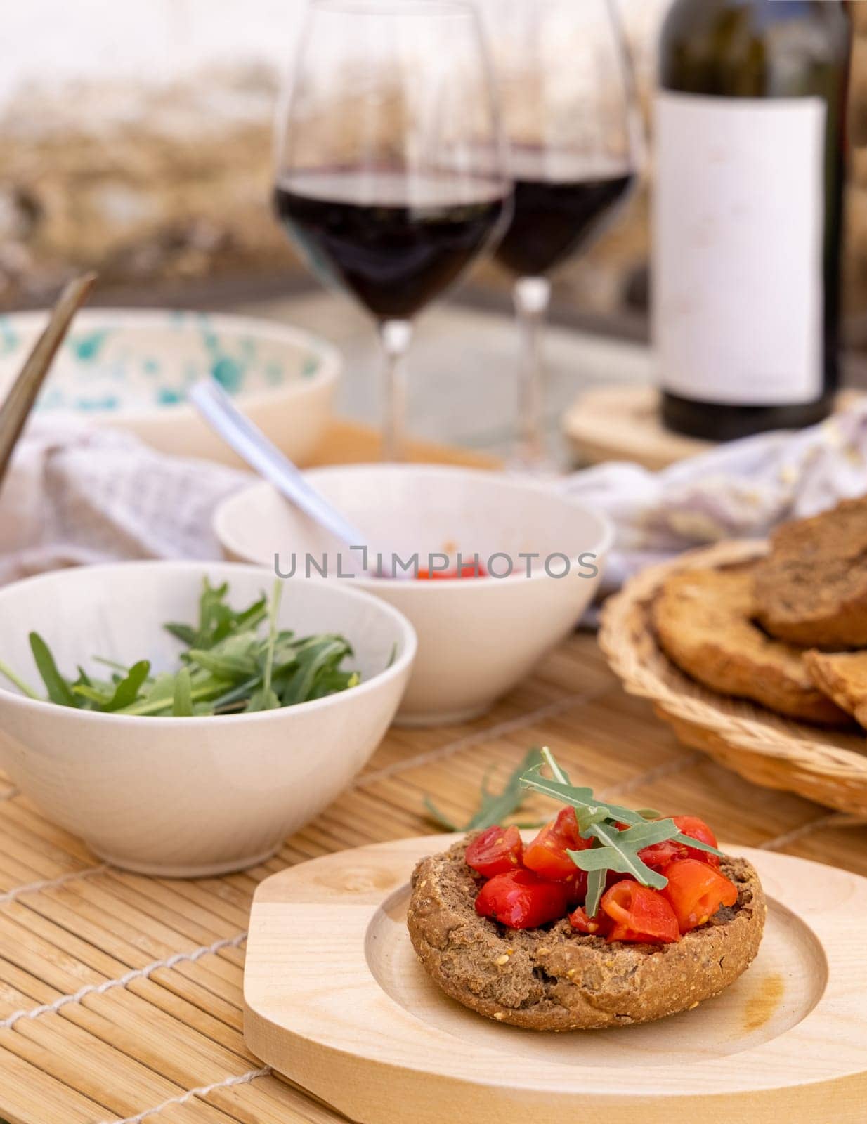 Italian summer appetizer Friselle with cherry tomatoes, oil and rucola served outdoor with glasses of red wine. Tipical Apulian Dried bread, made in Salento. Local cousine. Vegetarian food