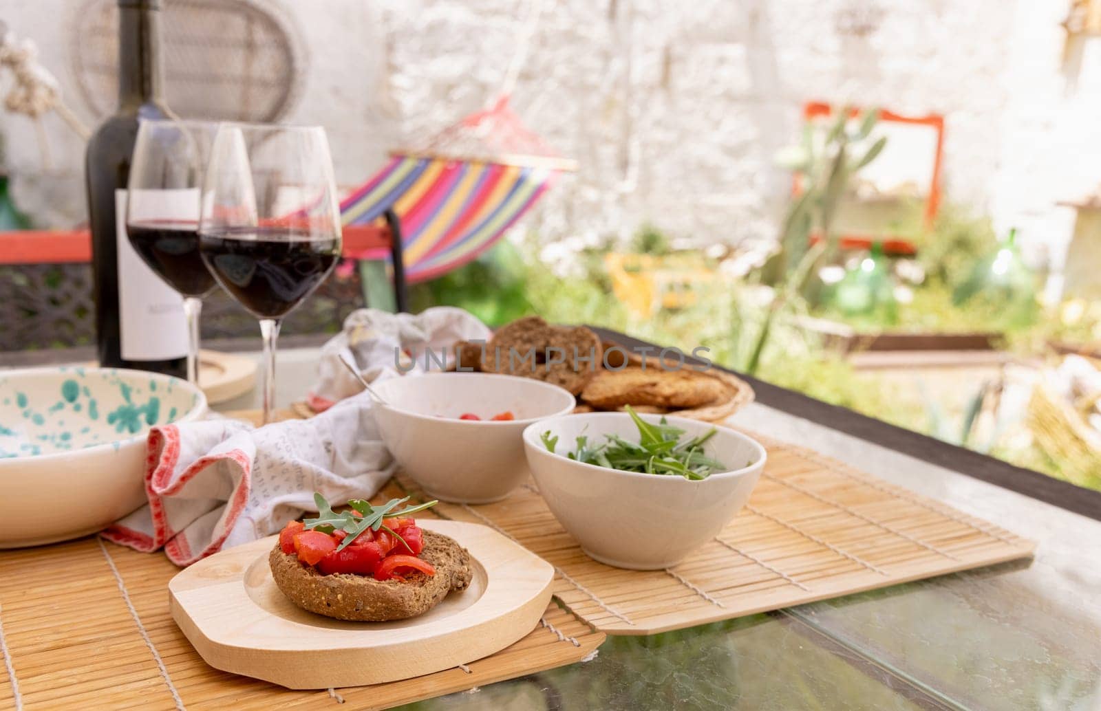 Italian summer appetizer Friselle with cherry tomatoes, oil and rucola served outdoor with glasses of red wine. Tipical Apulian Dried bread, made in Salento. Local cousine. Vegetarian food