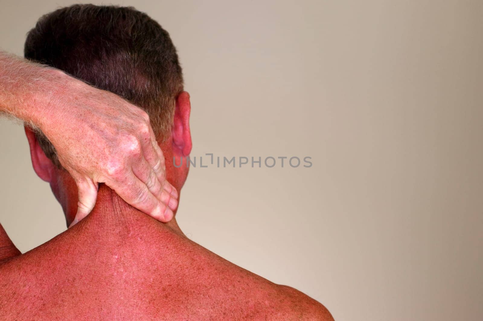 Adult male rubbing the back side of his neck with his hand as seen from a rear view close-up. Adult mature male 50 - 59 years massaging the back of his neck to help relive stress and tension.