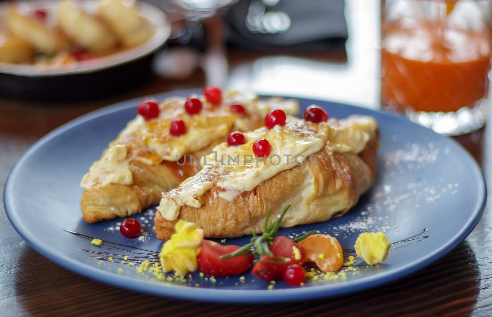 Freshly baked croissants with white, soft and sweet cream, red berries on a plate. Continental breakfast of two delicious croissants with cream on a dark wooden table in a restaurant