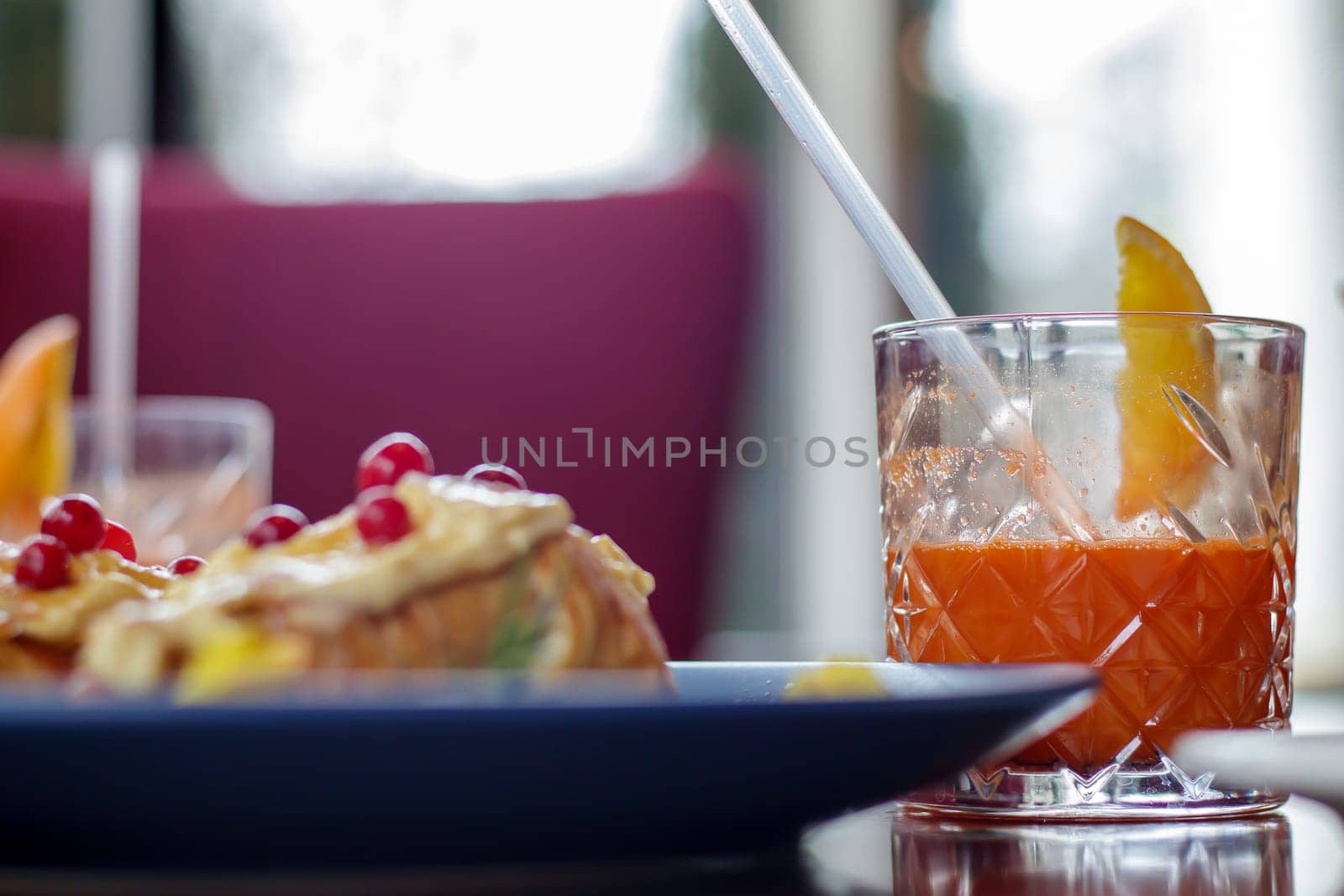 Freshly baked croissants with white sweet cream, red berries on a plate with freshly squeezed carrot juice. Continental breakfast on a dark wooden table in a restaurant