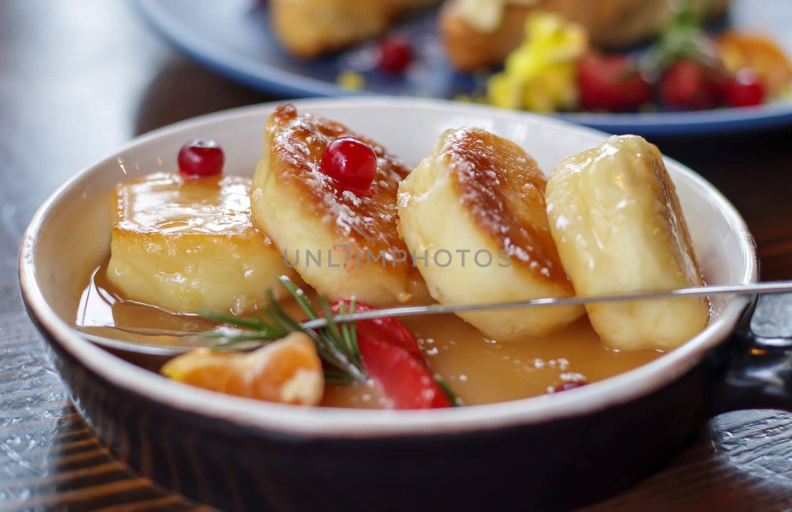 Close up fresh serving of four round paneer cheesecakes in salted caramel on a plate on the restaurant table in eco style. Cheesecakes or cottage cheese pancakes in a ceramic bowl. Morning breakfast