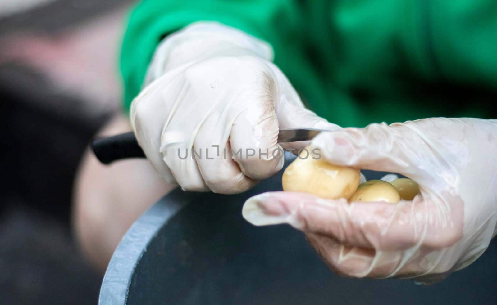 Woman's hands in white gloves peel raw new potatoes, close-up. Cleaning organic potatoes. Detail of female hands peeling fresh yellow potato with kitchen knife, food preparation concept