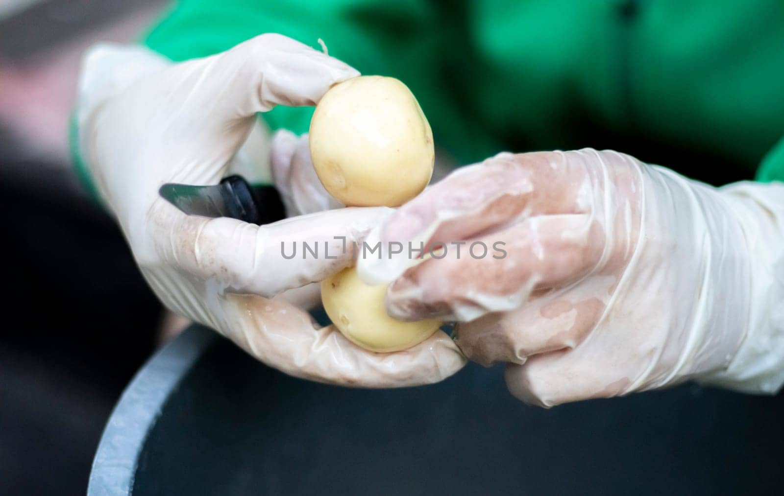 Woman's hands in white gloves peel raw new potatoes, close-up. Cleaning organic potatoes. Detail of female hands peeling fresh yellow potato with kitchen knife, food preparation concept