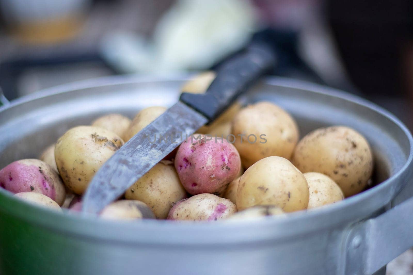 Stainless steel saucepan with raw new potatoes and a kitchen knife. Potatoes not peeled. Close-up of yellow and red skinned potatoes. Peeling potatoes in the kitchen on a wooden rustic table