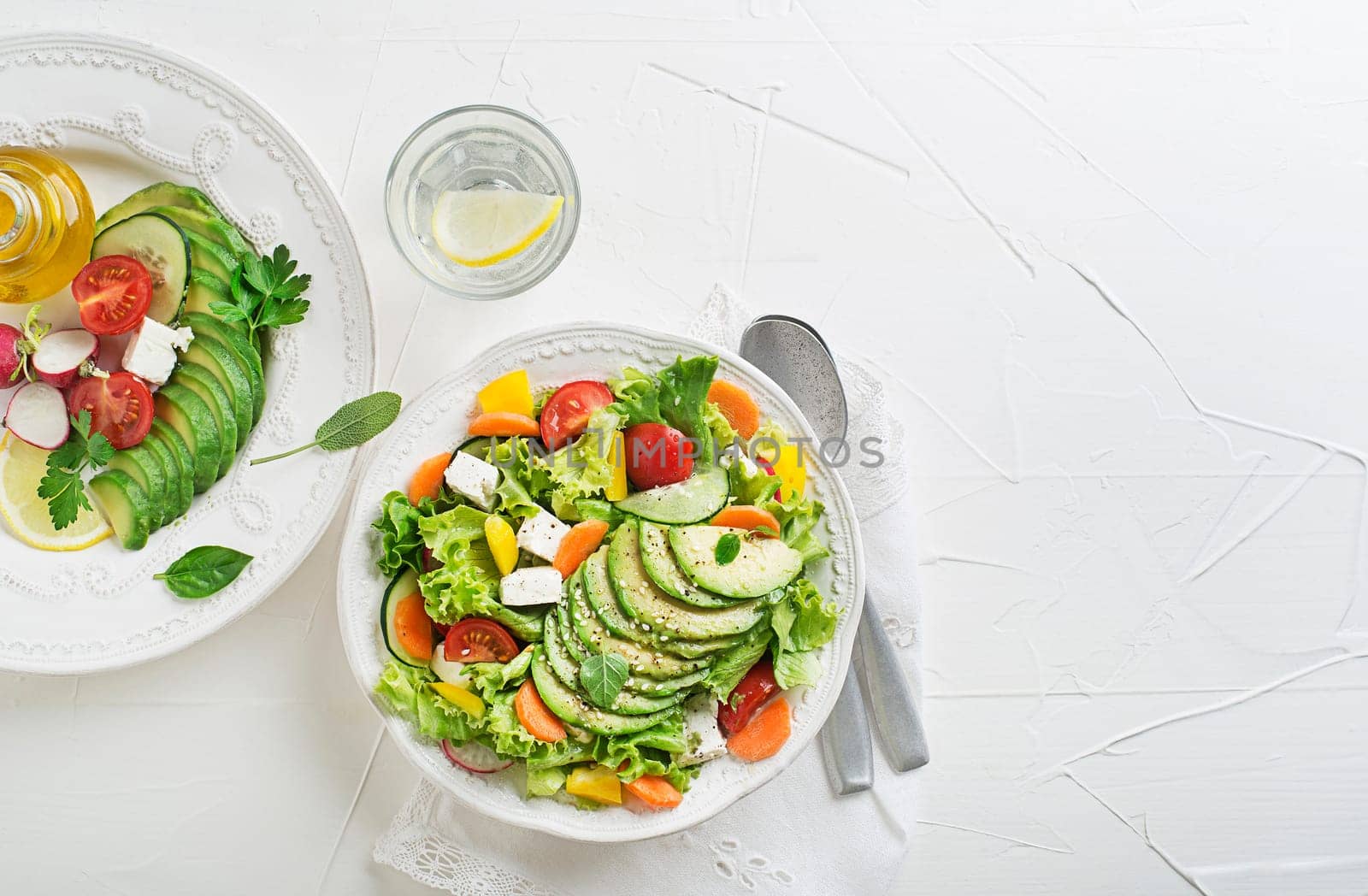 Healthy green salad with avocado, feta cheese and fresh vegetables on white background