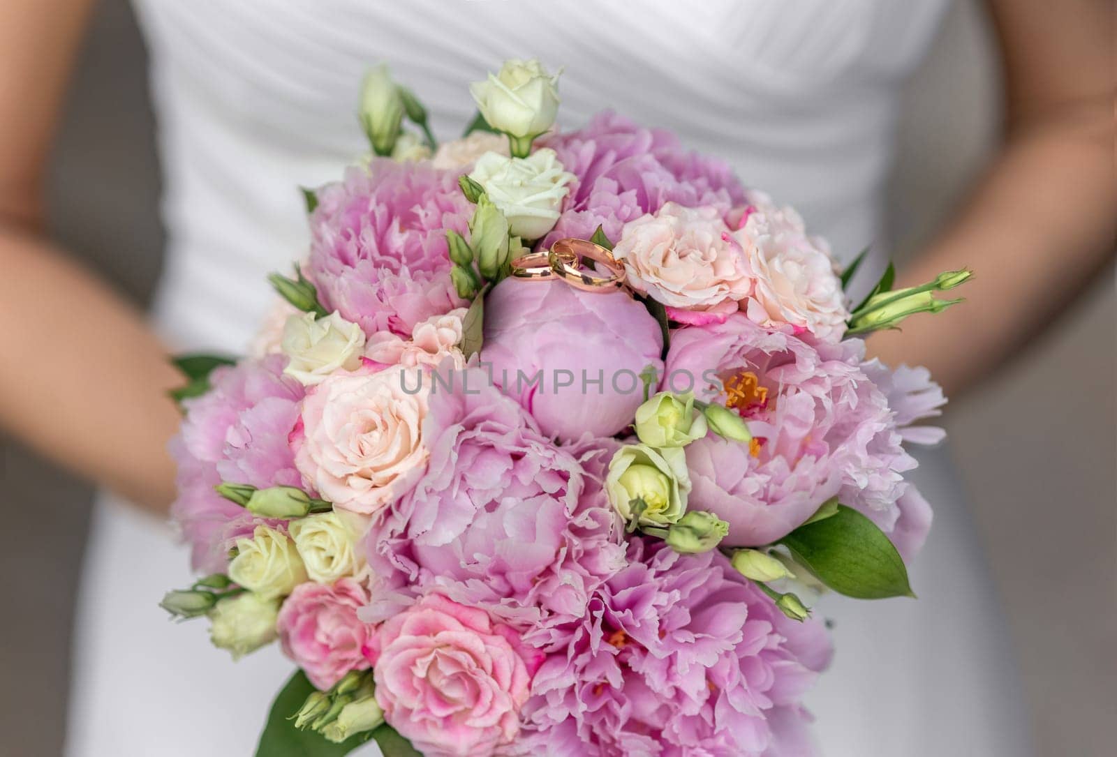 Bride's bouquet Beautiful of pink wedding flowers in the hands of the bride and rings on a pink bud