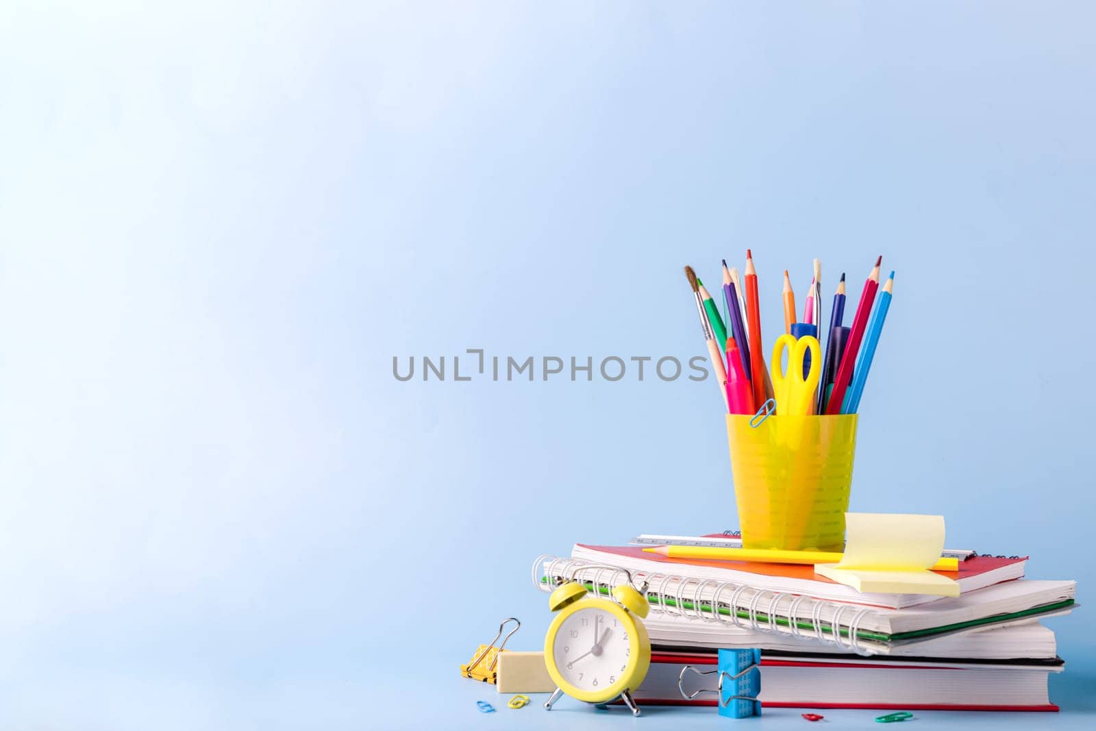 Many different various school, office supplies and stationery. Back to school concept. Notebook, book, pen, pencil, scissors, alarm clock, clock, sticker stand on a wooden table on a green background.