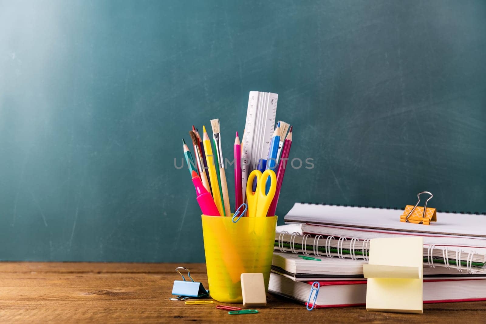 Many different various school, office supplies and stationery. Back to school concept. Notebook, book, pen, pencil, scissors, alarm clock, clock, sticker stand on a wooden table on a green background.