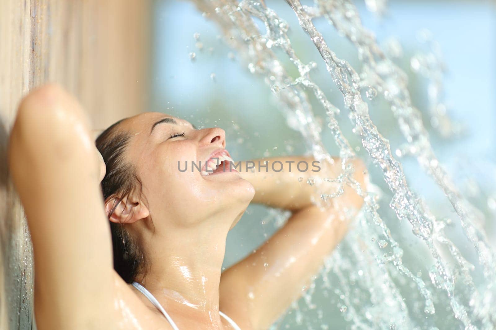 Happy woman enjoying and laughing under water jet in spa