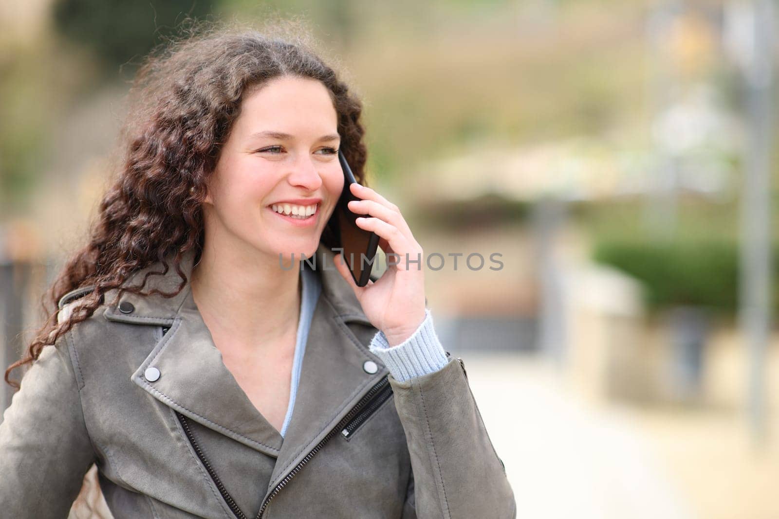 Happy woman talks on smart phone walking in the street