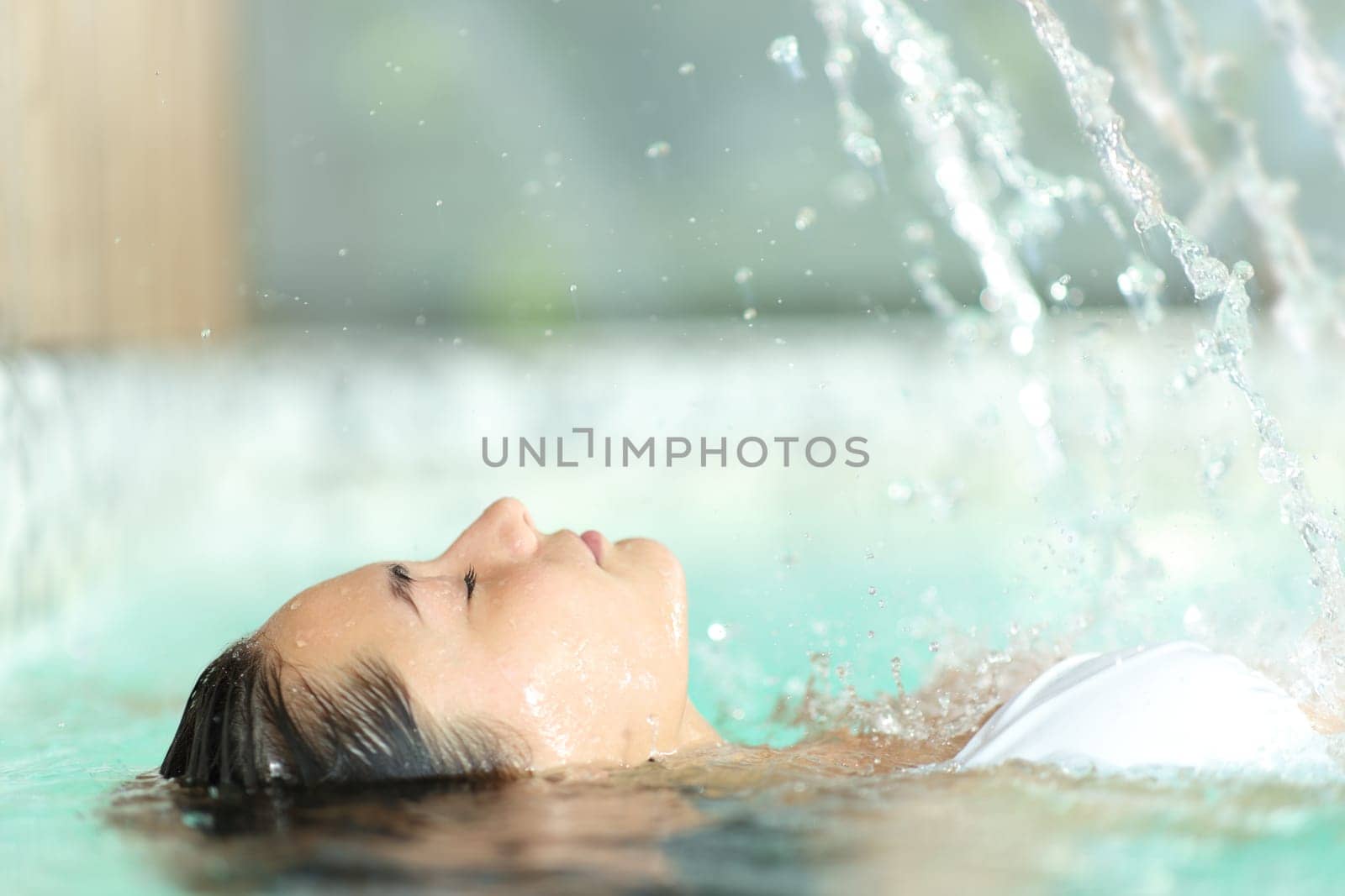 Side view portrait of a woman relaxing floating in spa pool water