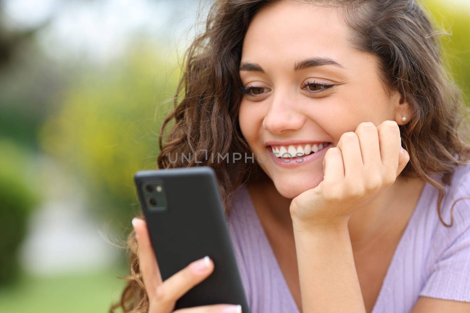 Happy woman checking smart phone smiling in a park