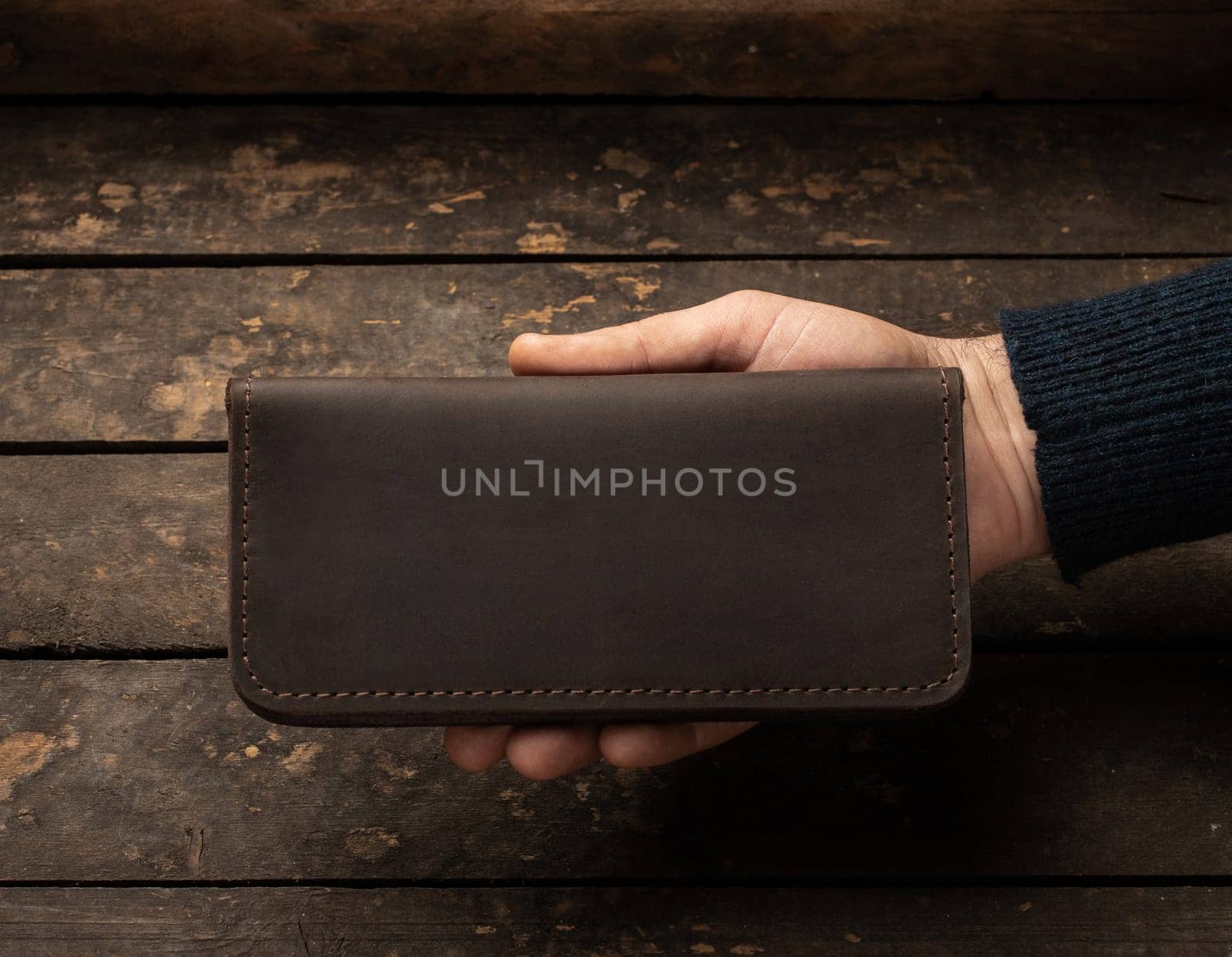 Leather men's wallet in a man's hand on a vintage wooden background. Flat lay. Place for text. Copyspace