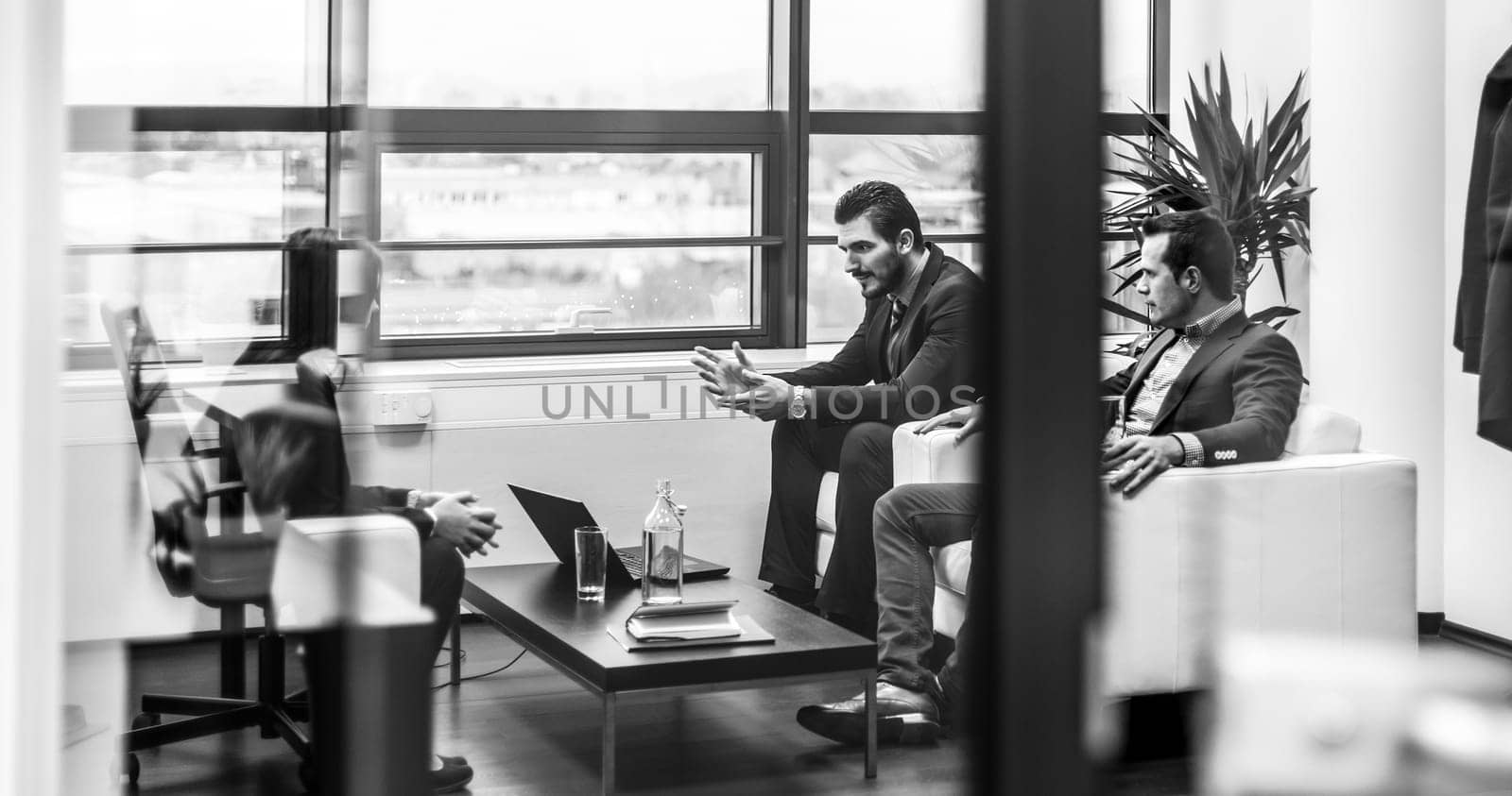 Businessmen interviewing female candidate for job in modern corporate office. Woman during job interview and two elegant members of management. Through glass view, black and white.