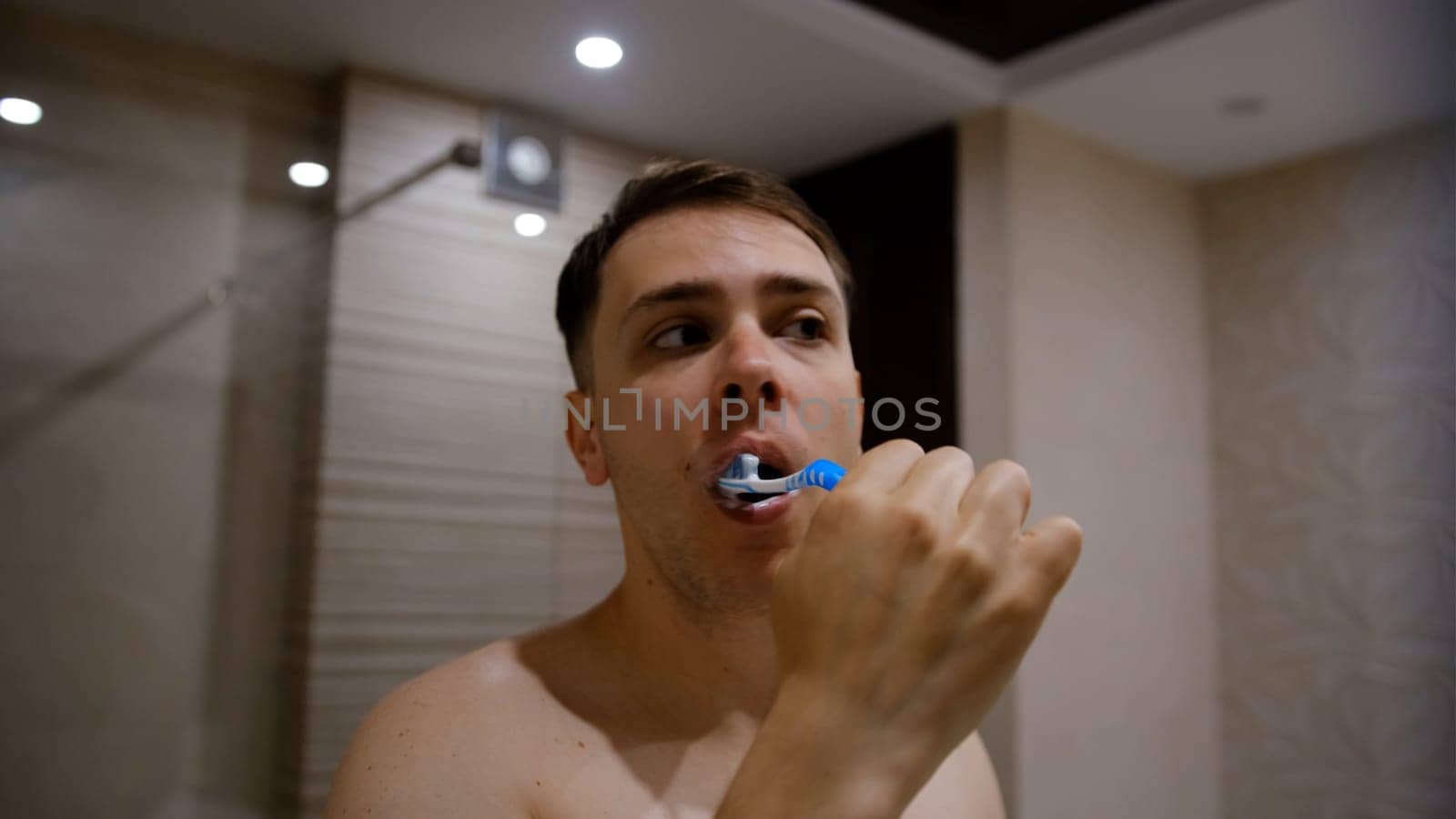 Young man brushing his teeth in bathroom. Beautiful interior.