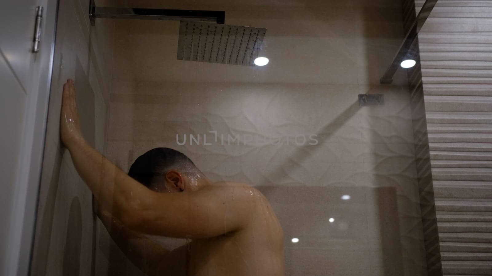 Man taking a shower washing hair under water falling from rain showerhead. Showering person at home lifestyle. Young adult body care morning routine