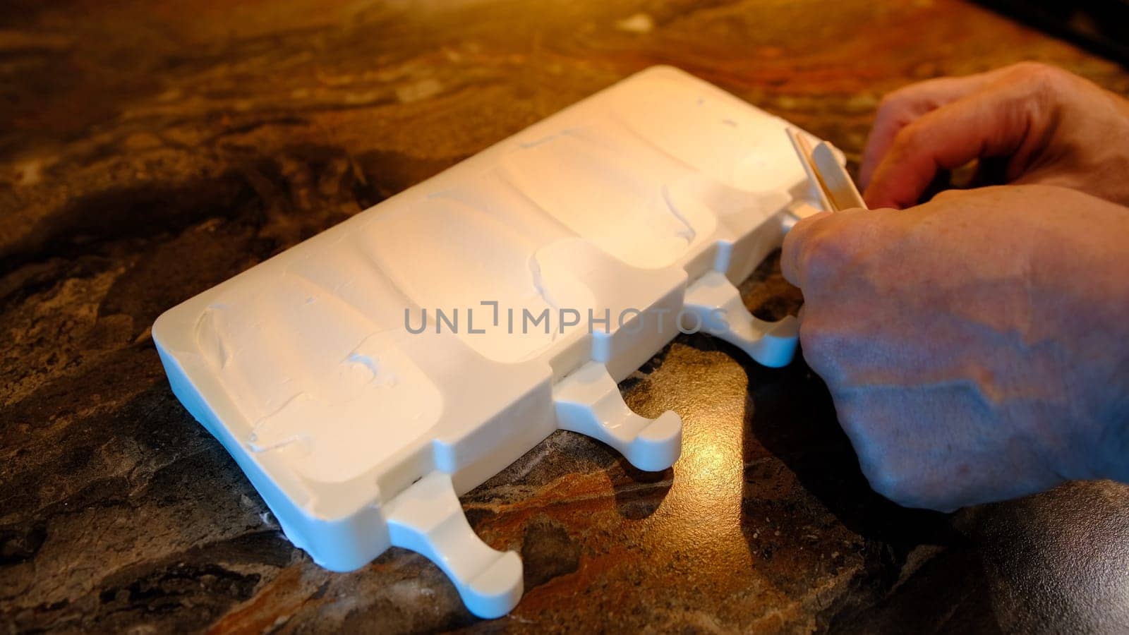 Making homemade popsicles. man pouring ice cream in freezer molds and put a stick inside