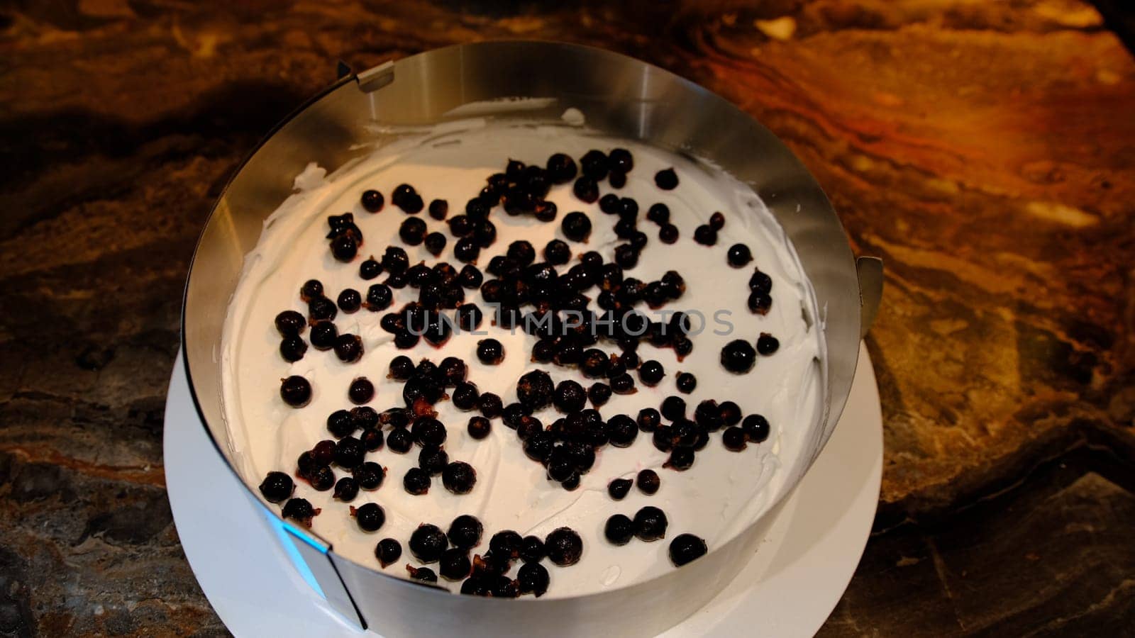 a male pastry chef puts a cake on cream with blueberry and press it. Slaps and flattens the sponge cake close up.