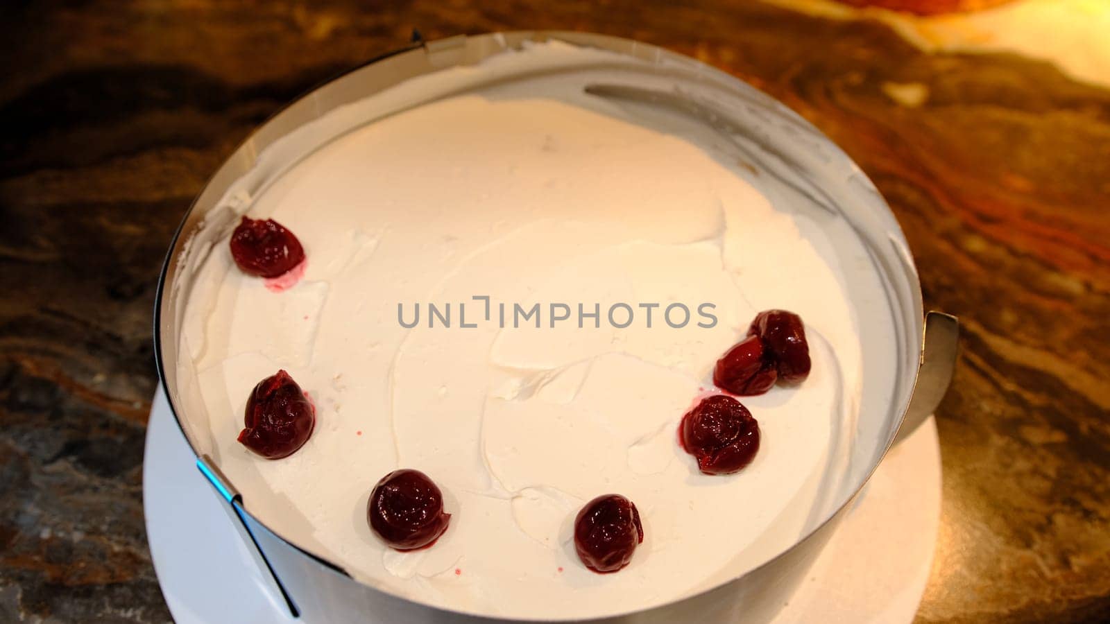A man puts cherry filling on biscuit cakes smeared with cream. On the plate are pieces of freshly baked biscuit. Cooking biscuit cake. Close-up