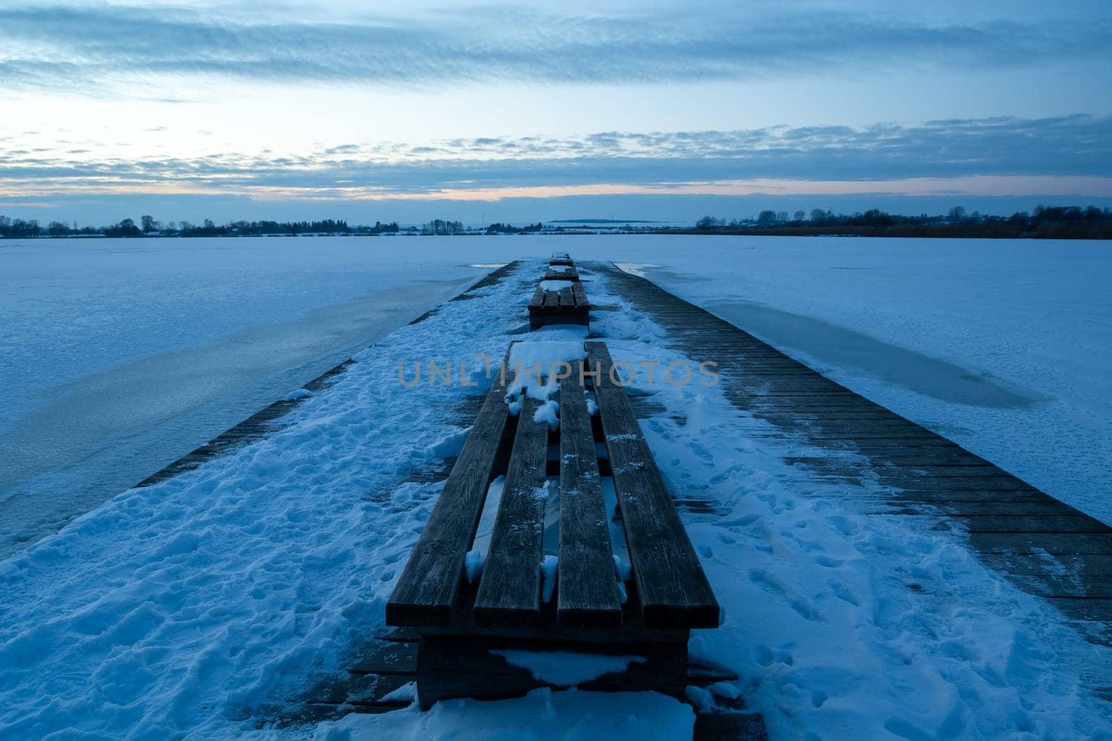 Wooden bench on a snow-covered pier and a frozen lake after sunset, Zoltance, Poland