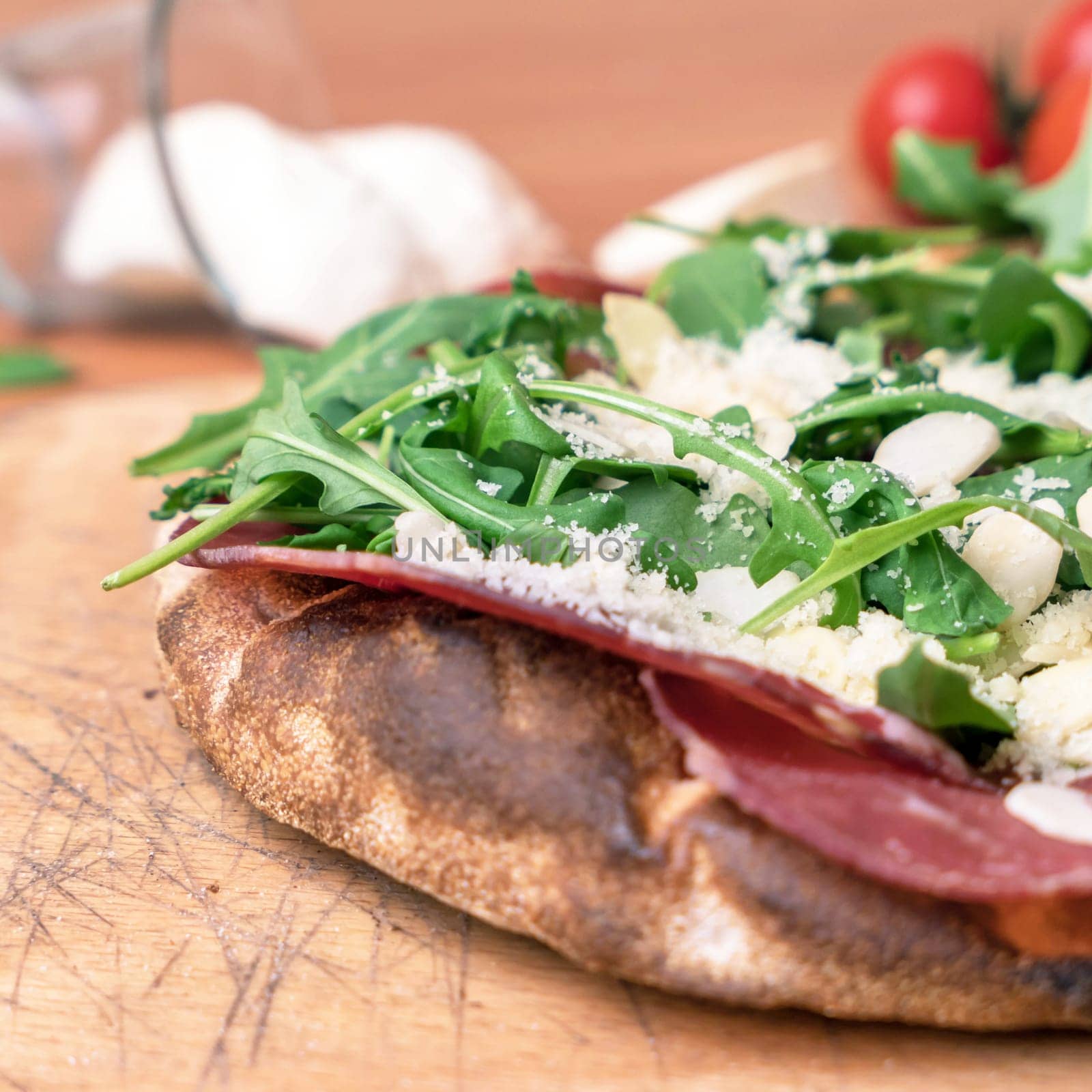 Close-up of a pizza with raw ham, parmesan cheese, almonds and rocket.
