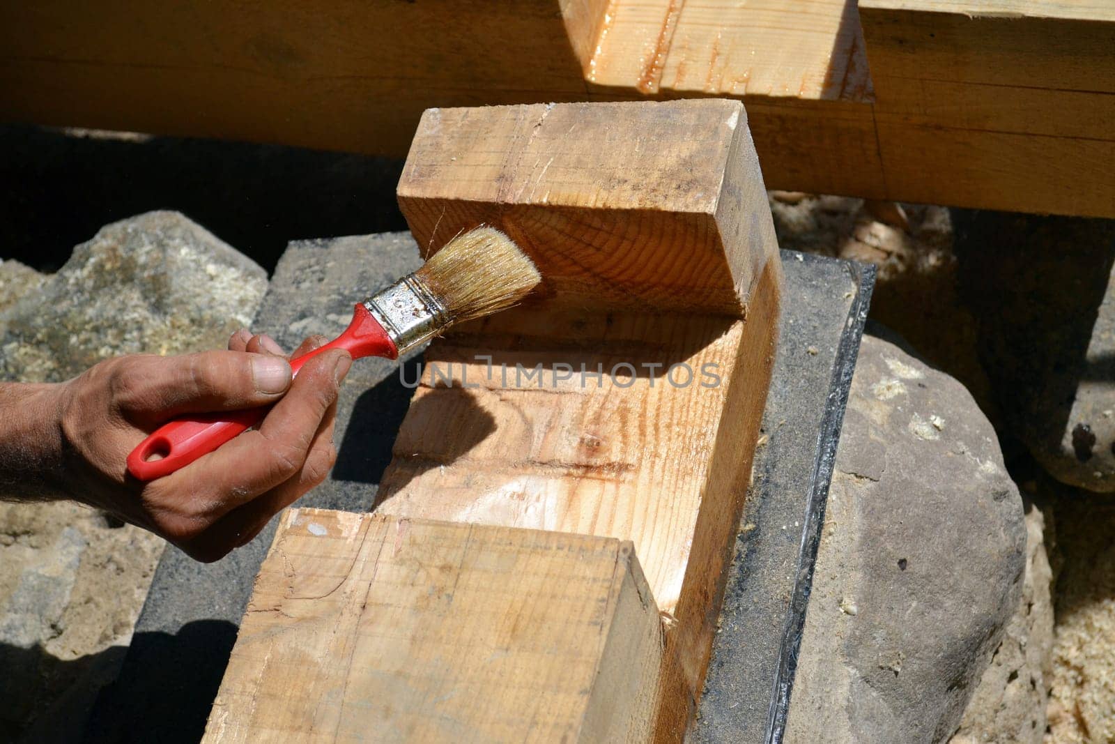 Hand of a worker oiling a wooden beam with a brush