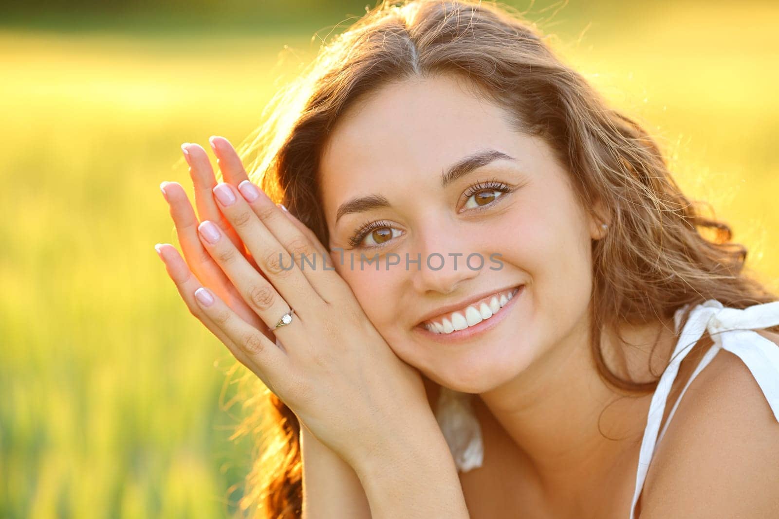 Engaged woman posing smiling looking at you showing ring in a field at sunset
