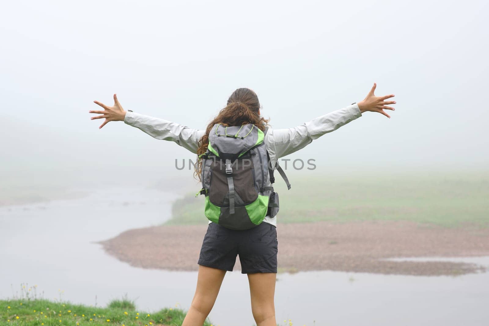 Back view portrait of a hiker outstretching arms in the mountain a foggy day